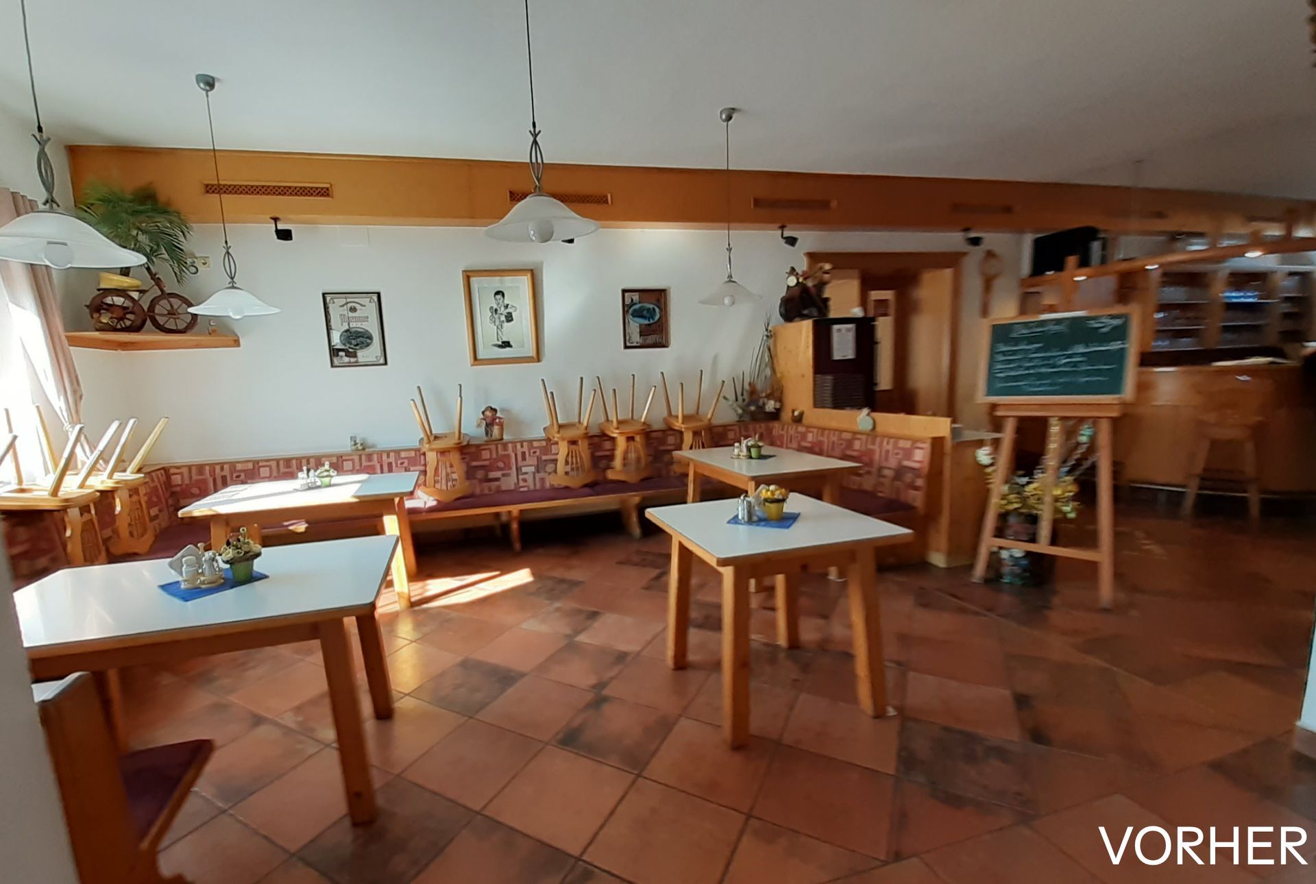 Innenansicht eines Restaurants mit Holztischen und -bänken, gefliestem Boden und einer kleinen Tafel auf einer Staffelei.