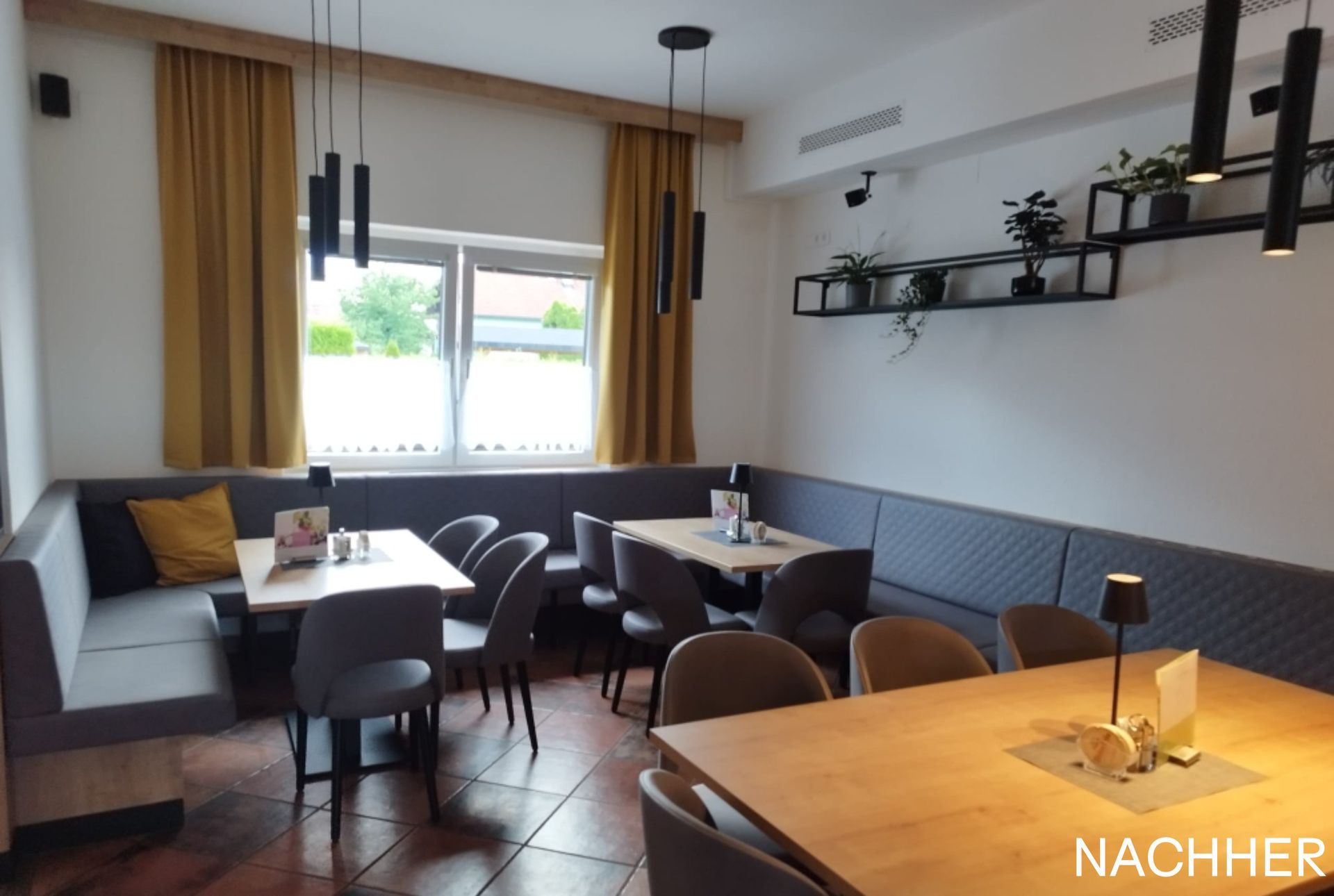 Restaurantinterieur mit Tischen, grauen und gelben Akzenten und Hängelampen.