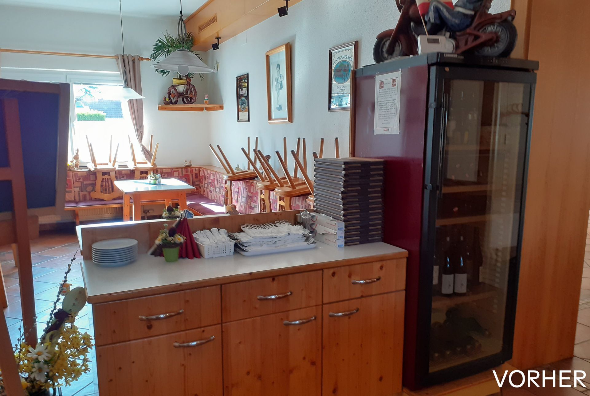 Innenansicht eines Restaurants: Holzschränke, Kühlvitrine, gestapelte Stühle, gedeckter Tisch, Kunstwerke an der Wand.