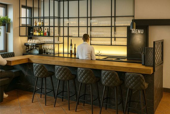 Bar mit Barkeeper hinter der Theke, schwarz-goldener Dekoration und Sitzgelegenheiten mit gesteppten Hockern.