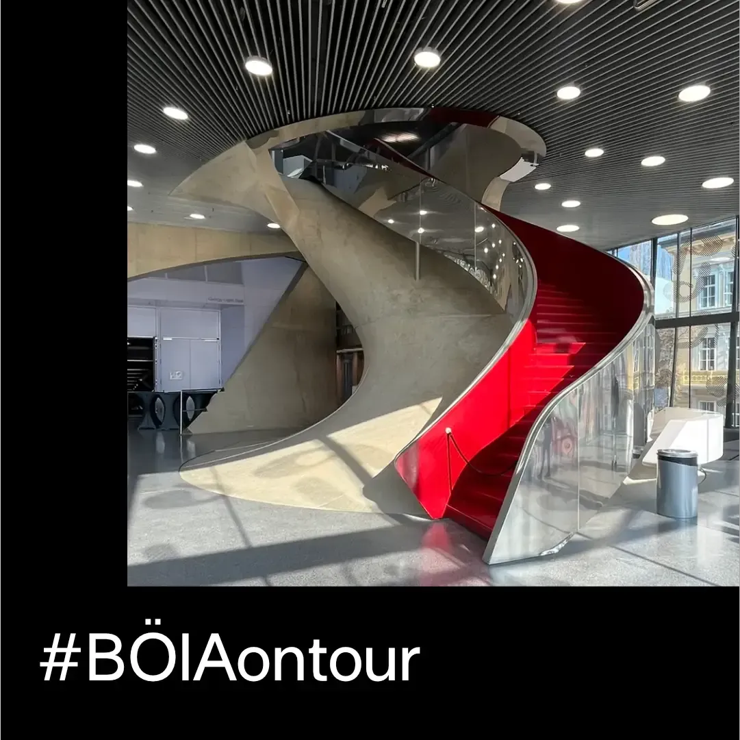 Eine moderne, rot-silberne Wendeltreppe in einem Gebäude; Hashtag #BÖlAontour.