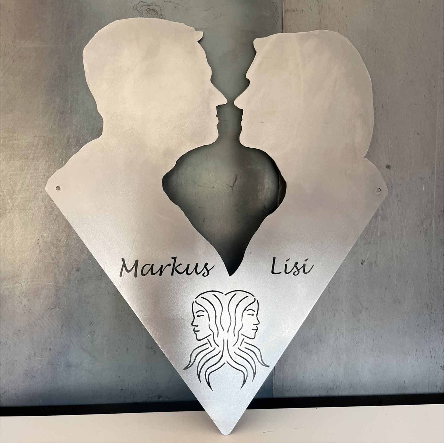 Metallkunstwerk mit zwei sich küssenden Profilen, dem Zwillinge-Symbol und den Namen „Markus“ und „Lisi“.