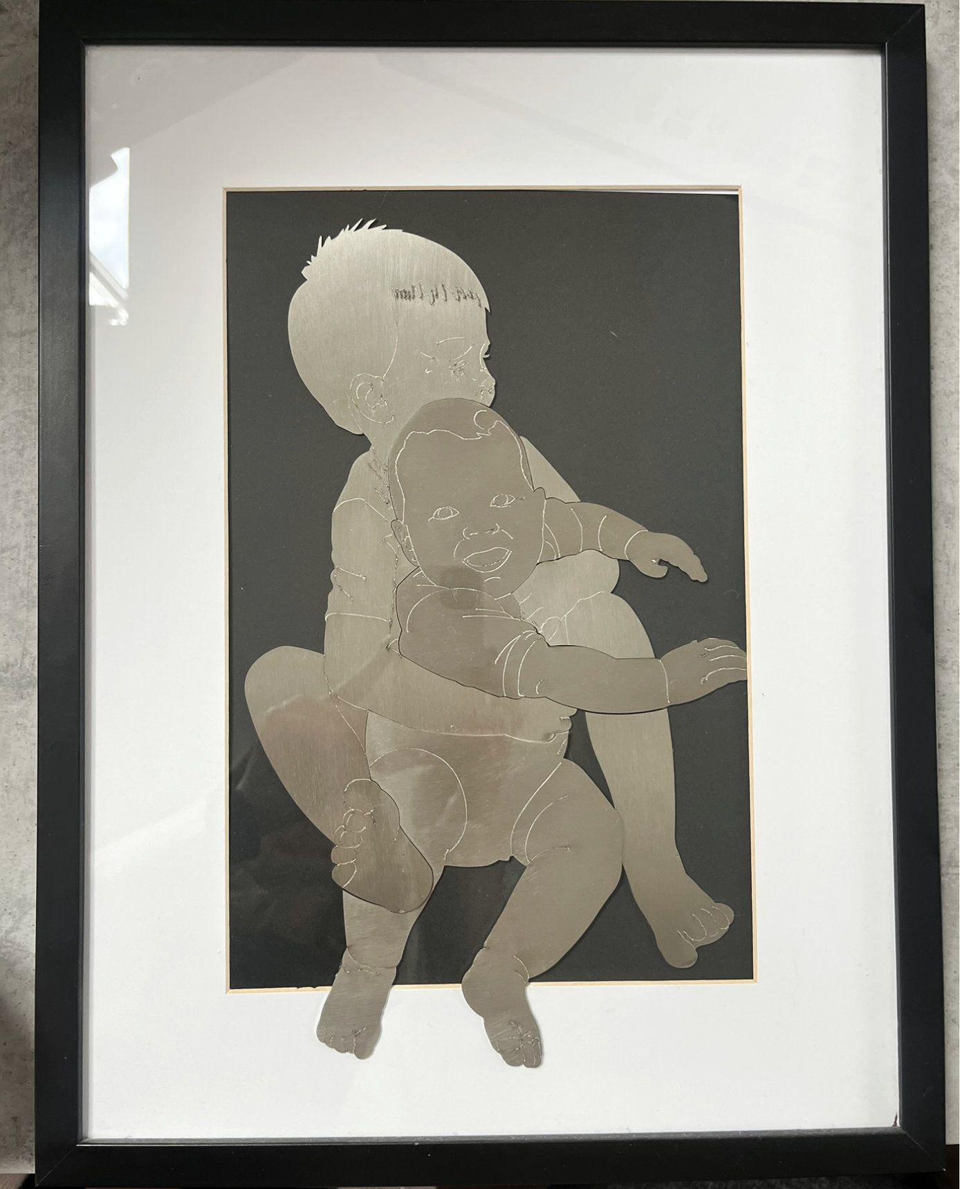 Gerahmtes Kunstwerk mit zwei sich überlappenden Babysilhouetten auf dunklem Hintergrund. 