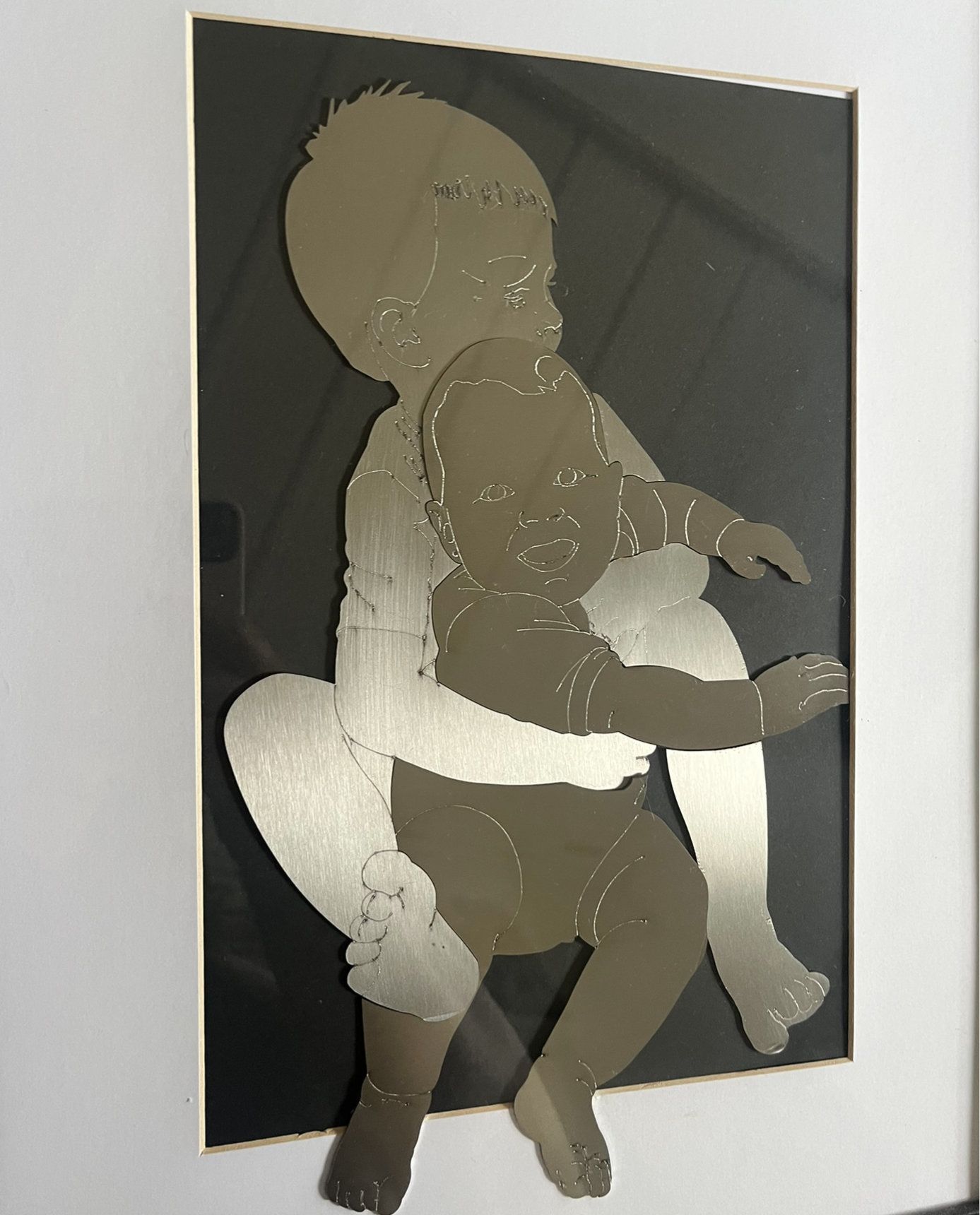 Metallene Silhouette eines Babys, das von einer Person gehalten wird, montiert auf schwarzem Hintergrund 