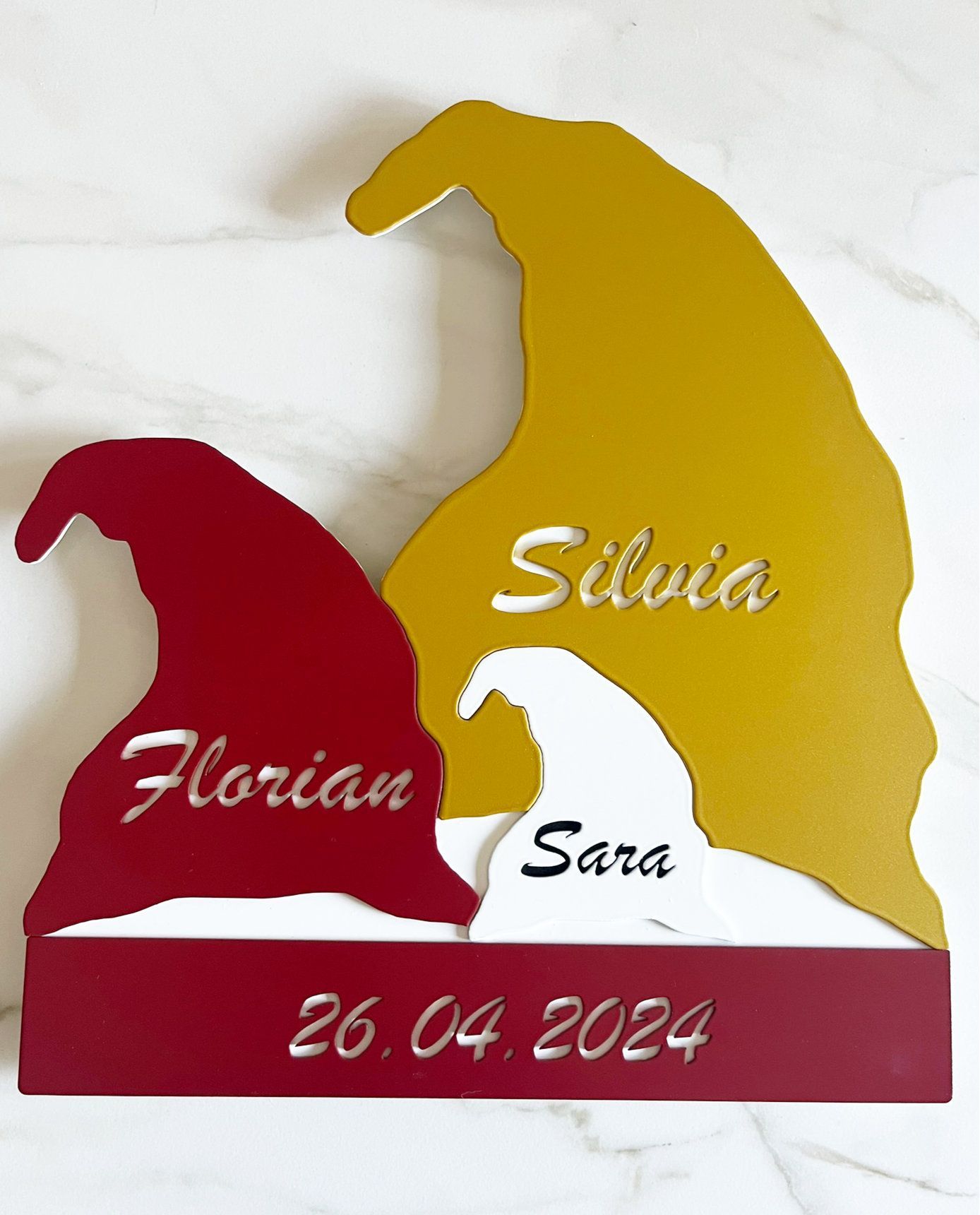 Holzfigur einer Zwergenfamilie mit Namen und Datum: rot, gold, weiß und mit rotem Sockel.