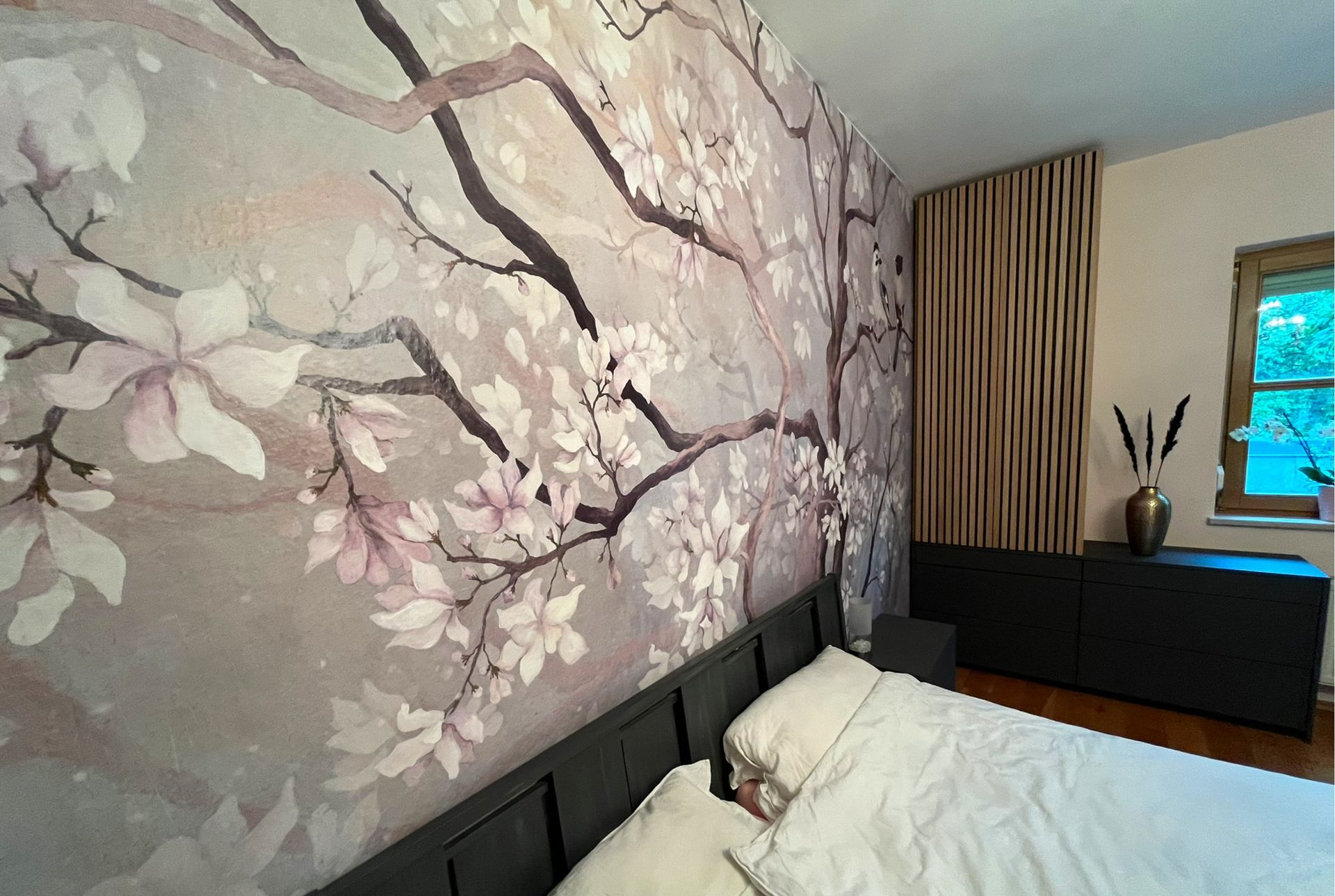 Schlafzimmer mit floralem Wandbild, schwarzem Bett, holzvertäfelter Wand und einem dunklen Schrank.