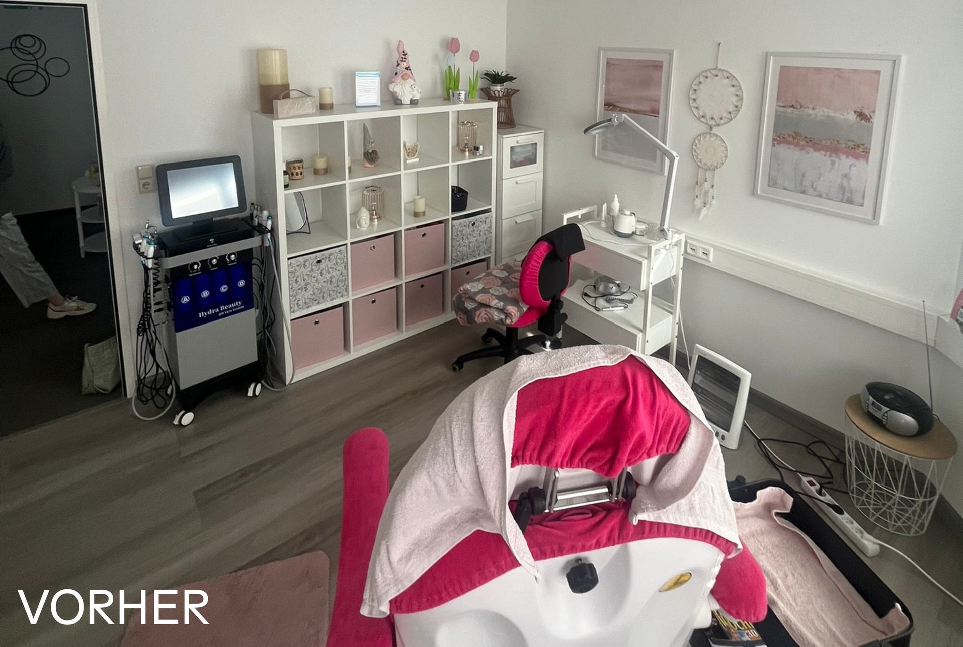 Ein Kosmetikbehandlungsraum mit Stuhl, Geräten und Regalen. Rosa-weiße Dekoration, Hinweisschild vor der Behandlung.