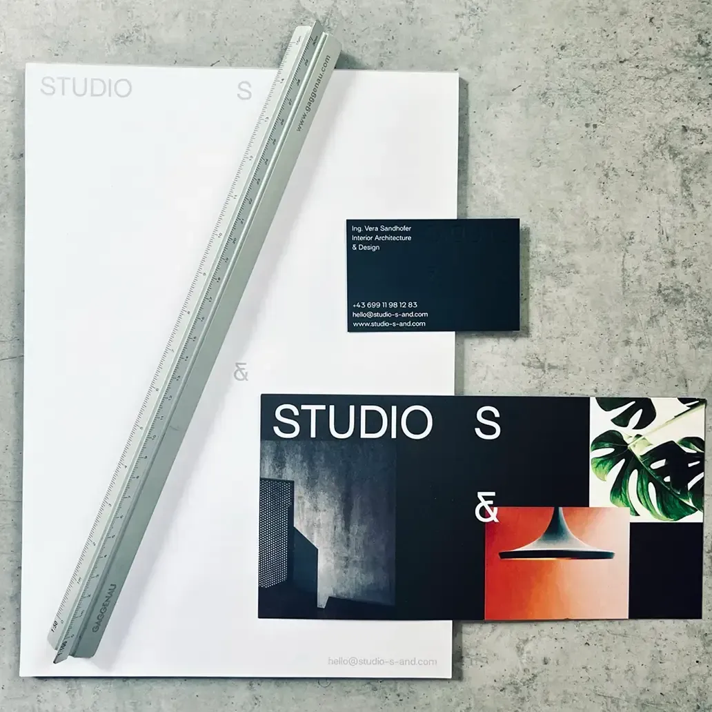 Studio S Branding: Briefpapier mit Logo auf weißem Grund, schwarze Visitenkarten, Lineal auf Beton.
