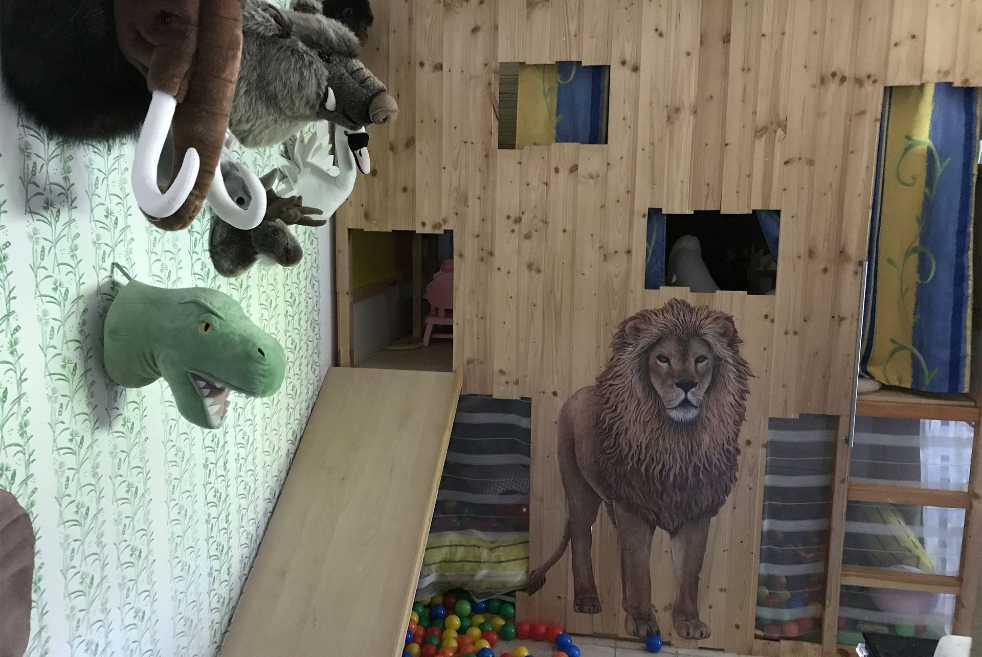 Spielzimmer mit Holzwänden, einer Rampe, einer Löwenfigur und Stofftieren.