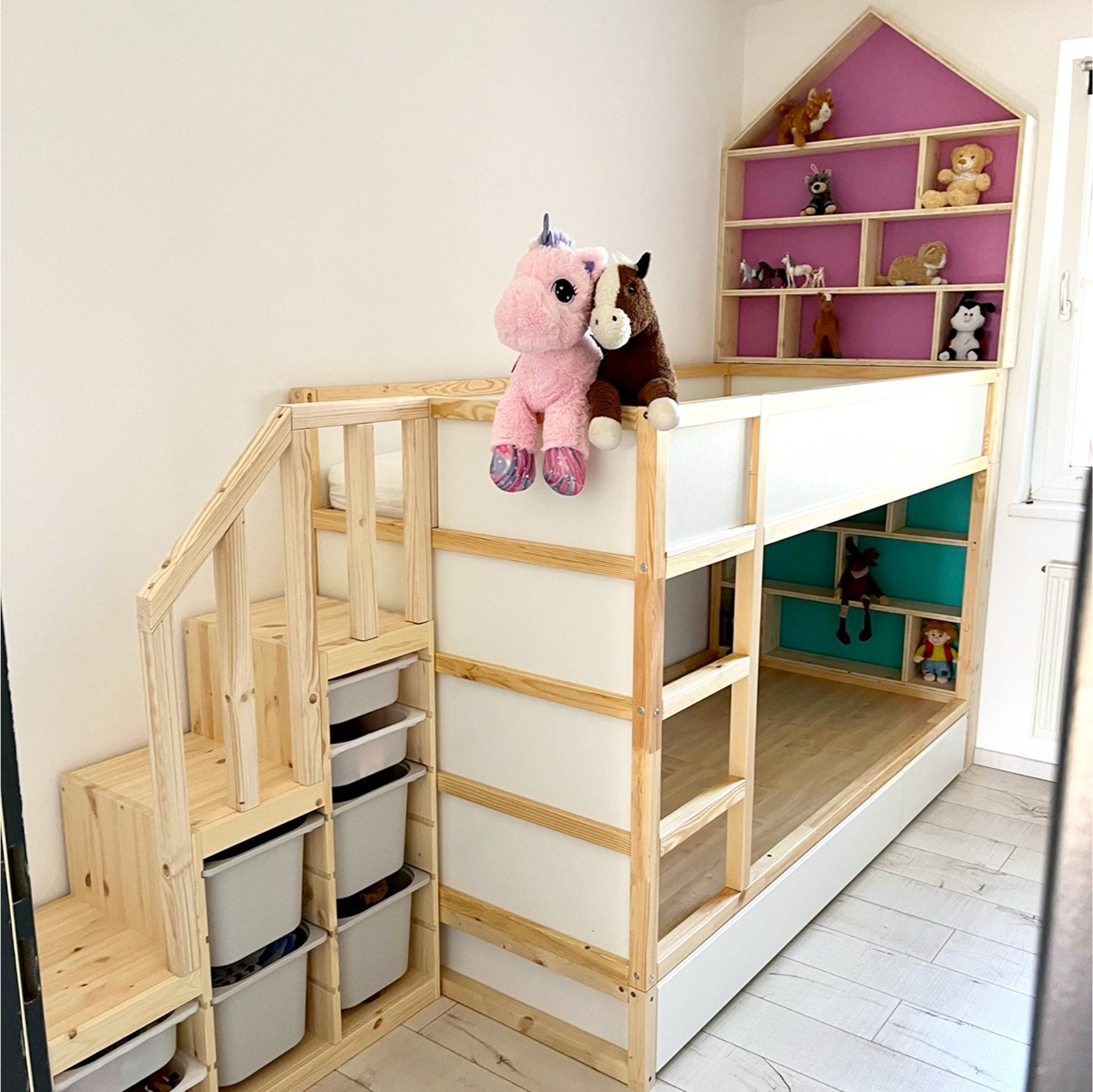 Ein hölzernes Etagenbett mit Treppe, Stauraum und einem hausförmigen Bücherregal voller Spielzeug.