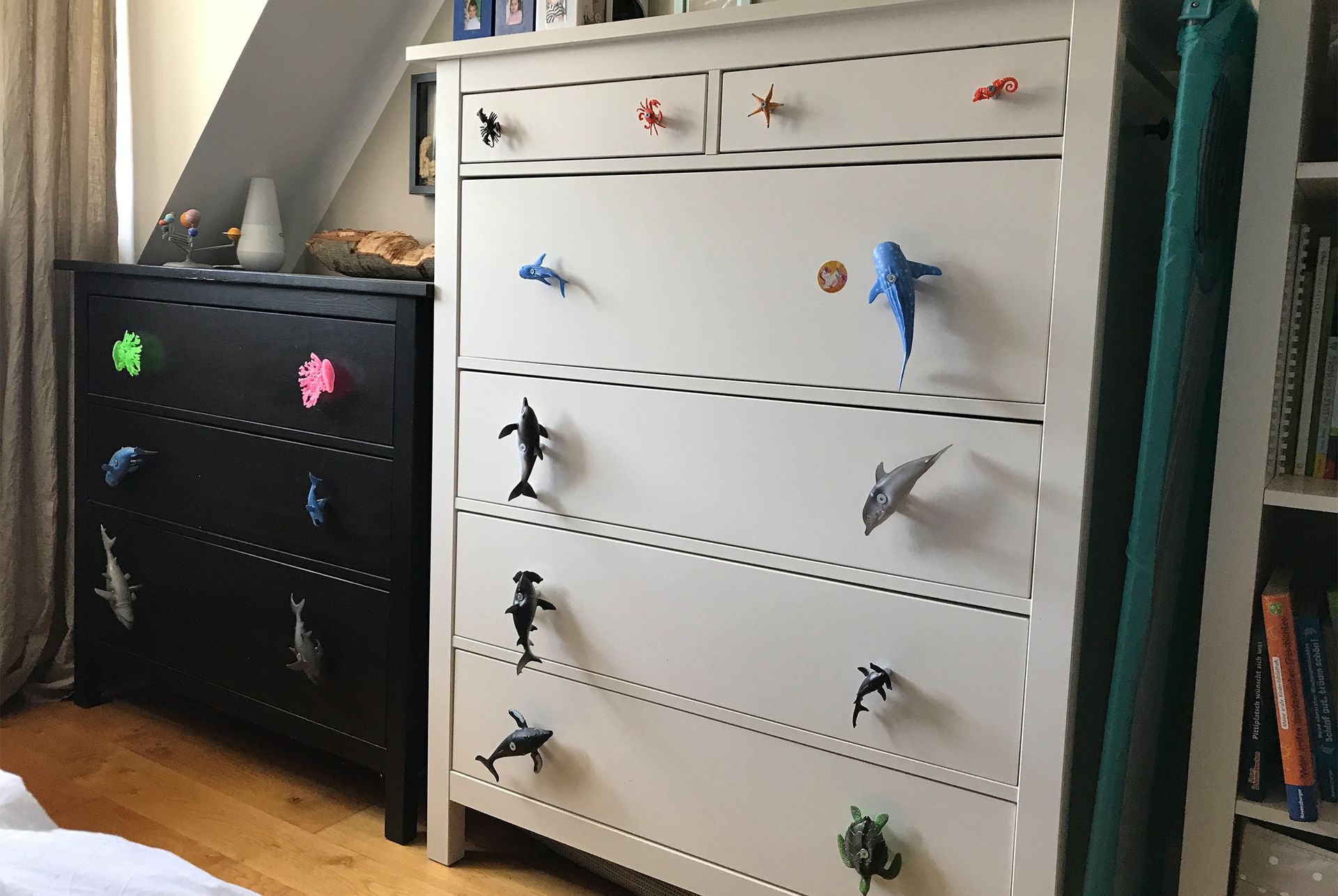 Zwei Kommoden, eine schwarze und eine weiße, verziert mit Spielzeug-Meerestieren als Schubladengriffe.