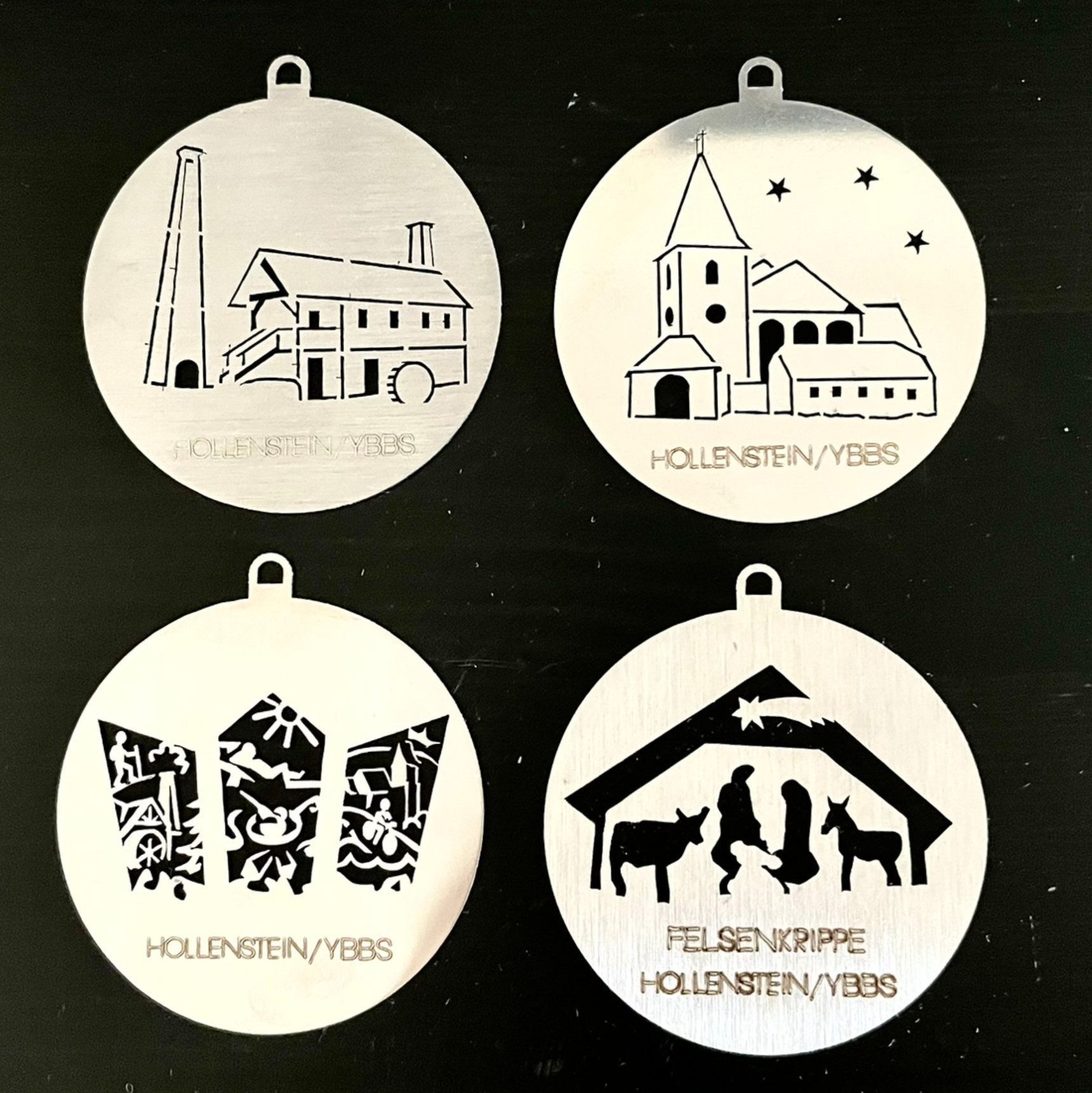 Vier metallene Weihnachtsornamente mit lasergeschnittenen Motiven: eine Kirche, ein abstraktes Motiv und eine Krippenszene.