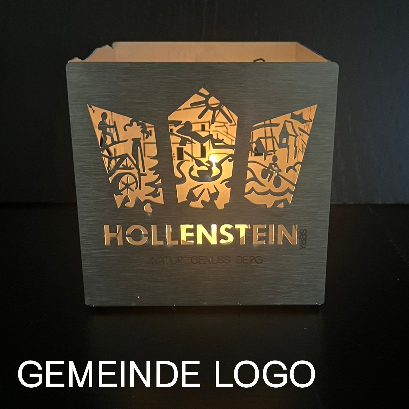 Beleuchteter Teelichthalter mit „HOLLENSTEIN“-Logo. Graue Schachtel mit ausgeschnittenem Muster