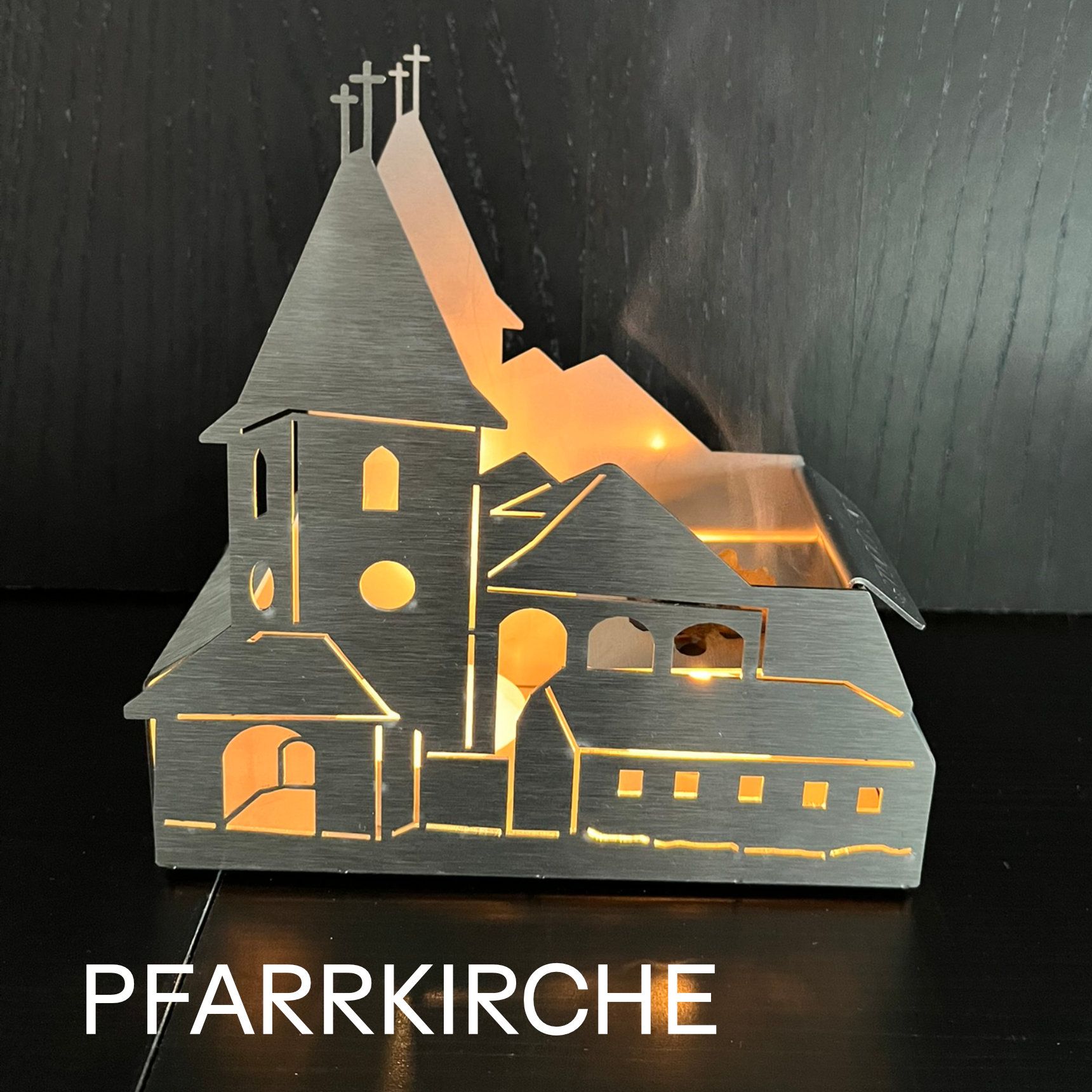 Silhouette einer von innen beleuchteten Kirche, darunter das Wort „Pfarrkirche“.