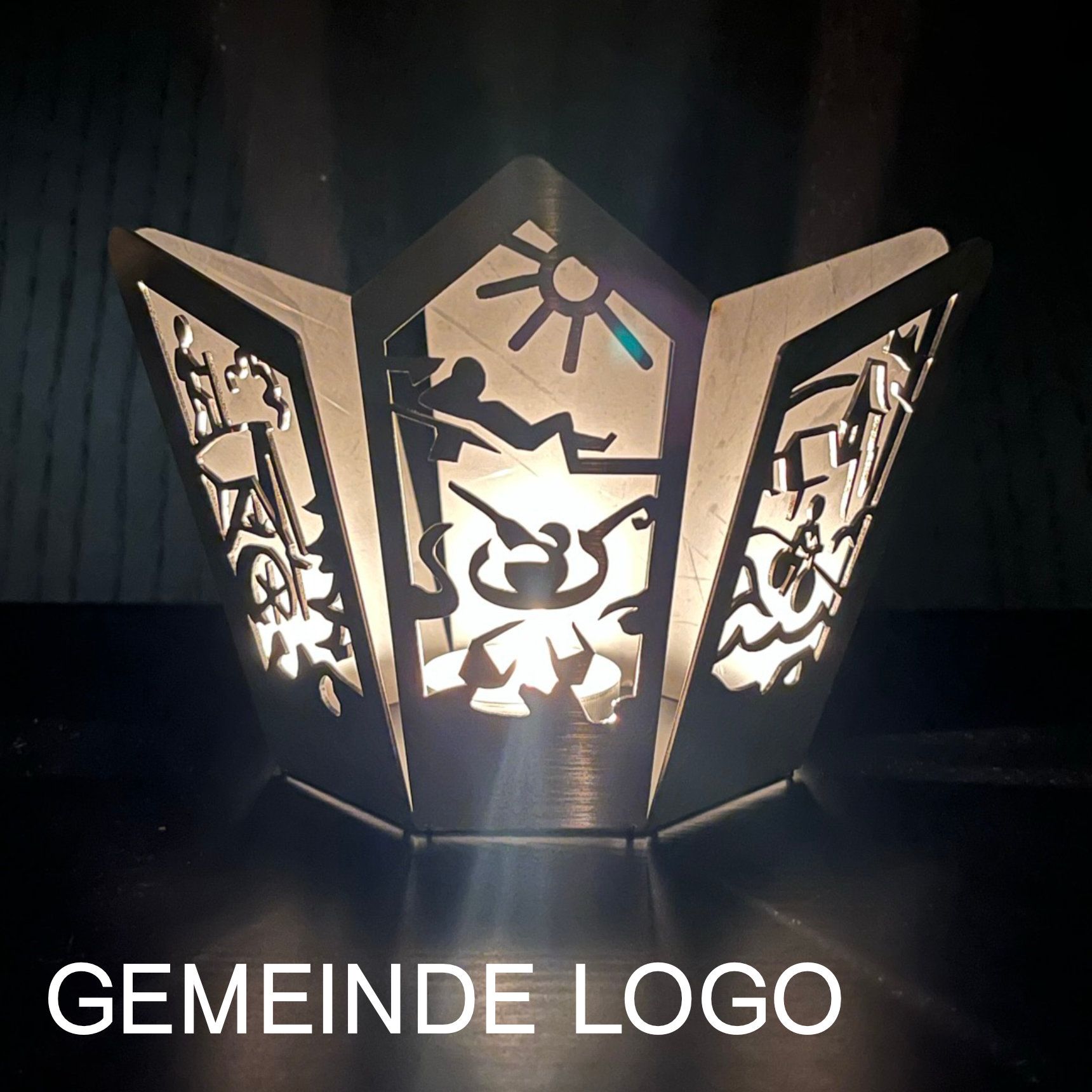 Metalllaterne mit ausgeschnittenen Motiven von Sonne, Figuren und Symbolen; leuchtet von innen. „Gemeinde Logo“ darunter.