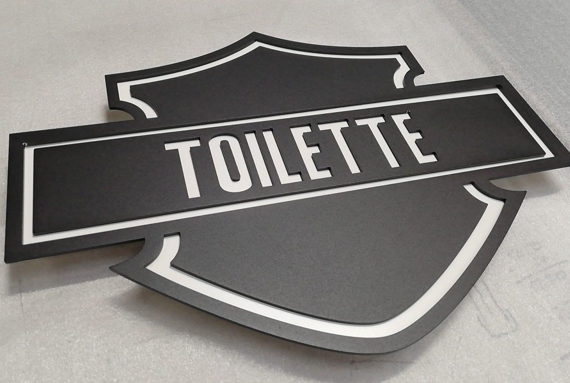Schwarz-weißes Schild mit der Aufschrift „TOILETTE“ in Schildform, vermutlich für ein Badezimmer.