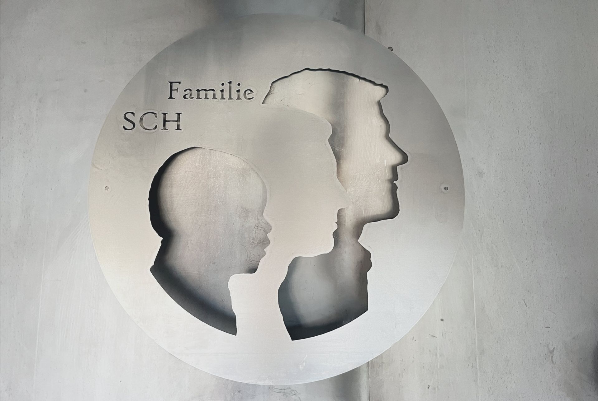 Ein kreisrunder Metallausschnitt mit den Silhouetten von Menschen, mit der Aufschrift „Familie SCH“.