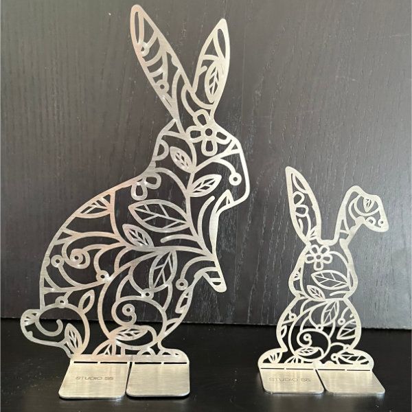 Zwei lasergeschnittene Hasenfiguren aus Metall mit Blumen- und Blattmustern.