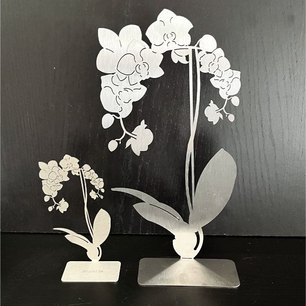 Zwei Orchideenskulpturen aus Metall: eine große und eine kleinere, vor dunklem Hintergrund.