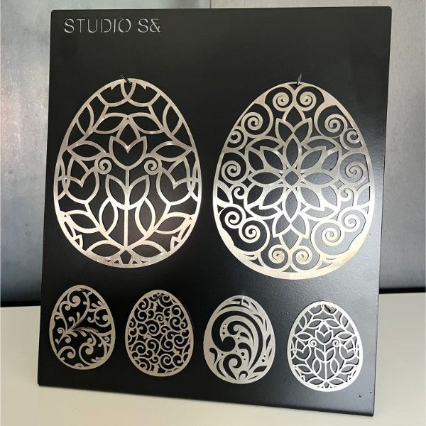 Silberne Ostereierdekorationen auf einem schwarzen Präsentationsbrett, kunstvolle Blumenmuster. Studio SS-Logo.