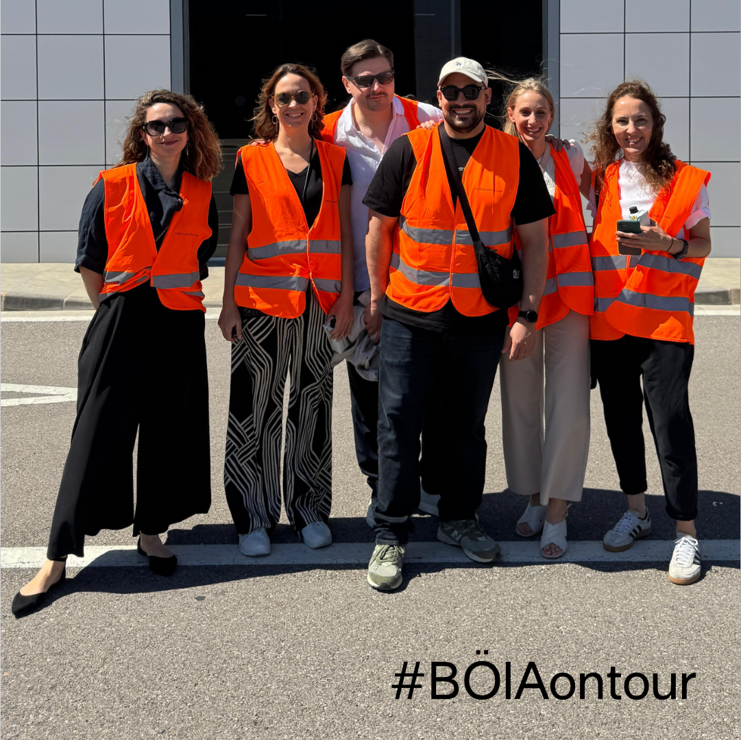 Eine Gruppe von sieben Personen in orangefarbenen Westen posiert vor einem Gebäude.