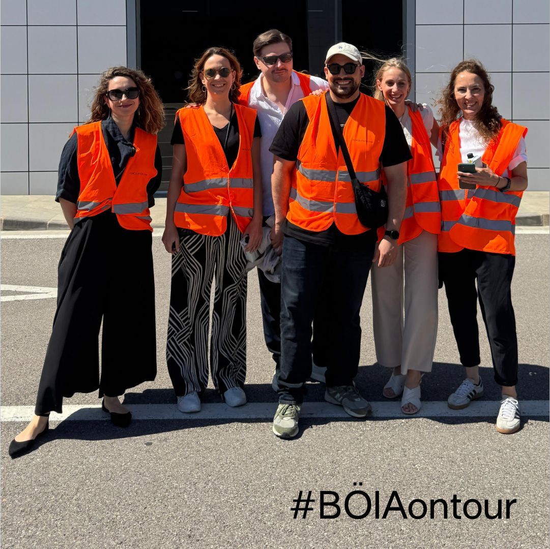 Eine Gruppe von sieben Personen in orangefarbenen Westen posiert vor einem Gebäude.