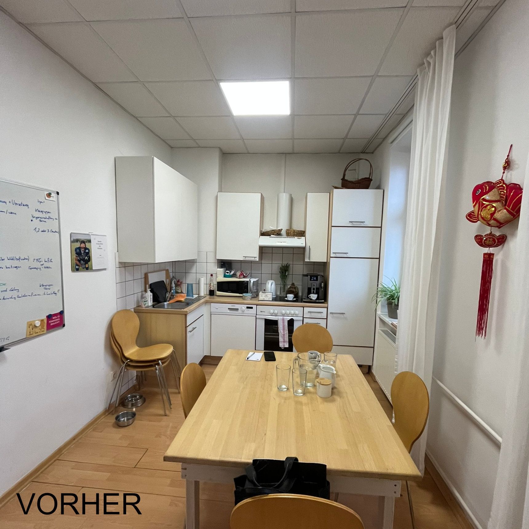 Küche mit Holztisch und -stühlen, weißen Schränken und einer Mikrowelle. „VORHER“-Etikett unten links.