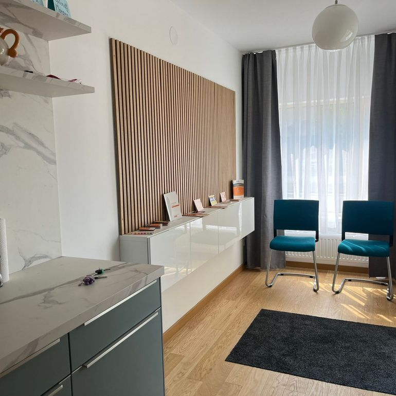 Wartezimmer mit blauen Stühlen, moderner Einrichtung und einer Akzentwand aus Holz.