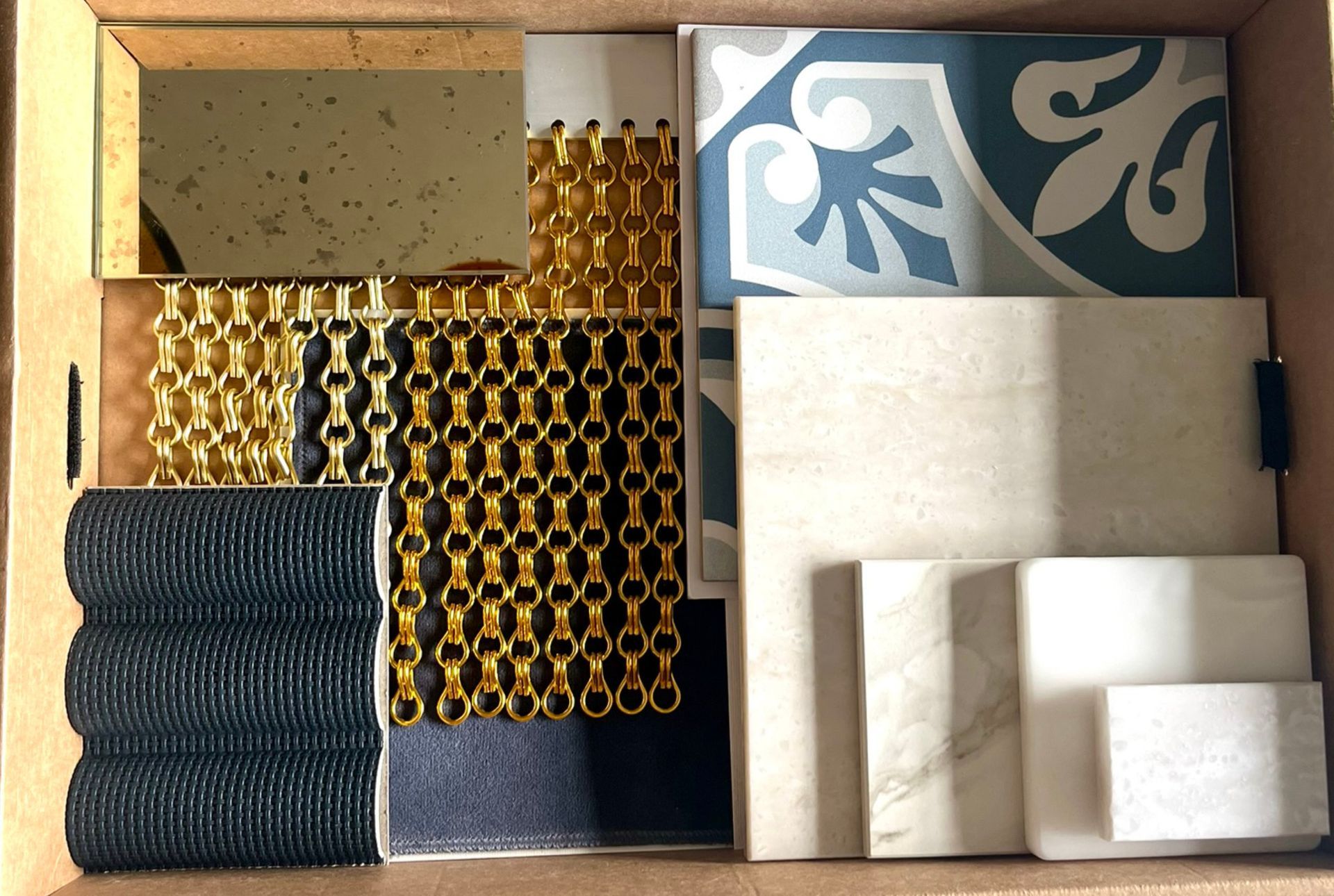 Muster von Fliesen und Dekorationsmaterialien in einem Karton, darunter Blau-, Gold- und Cremetöne.