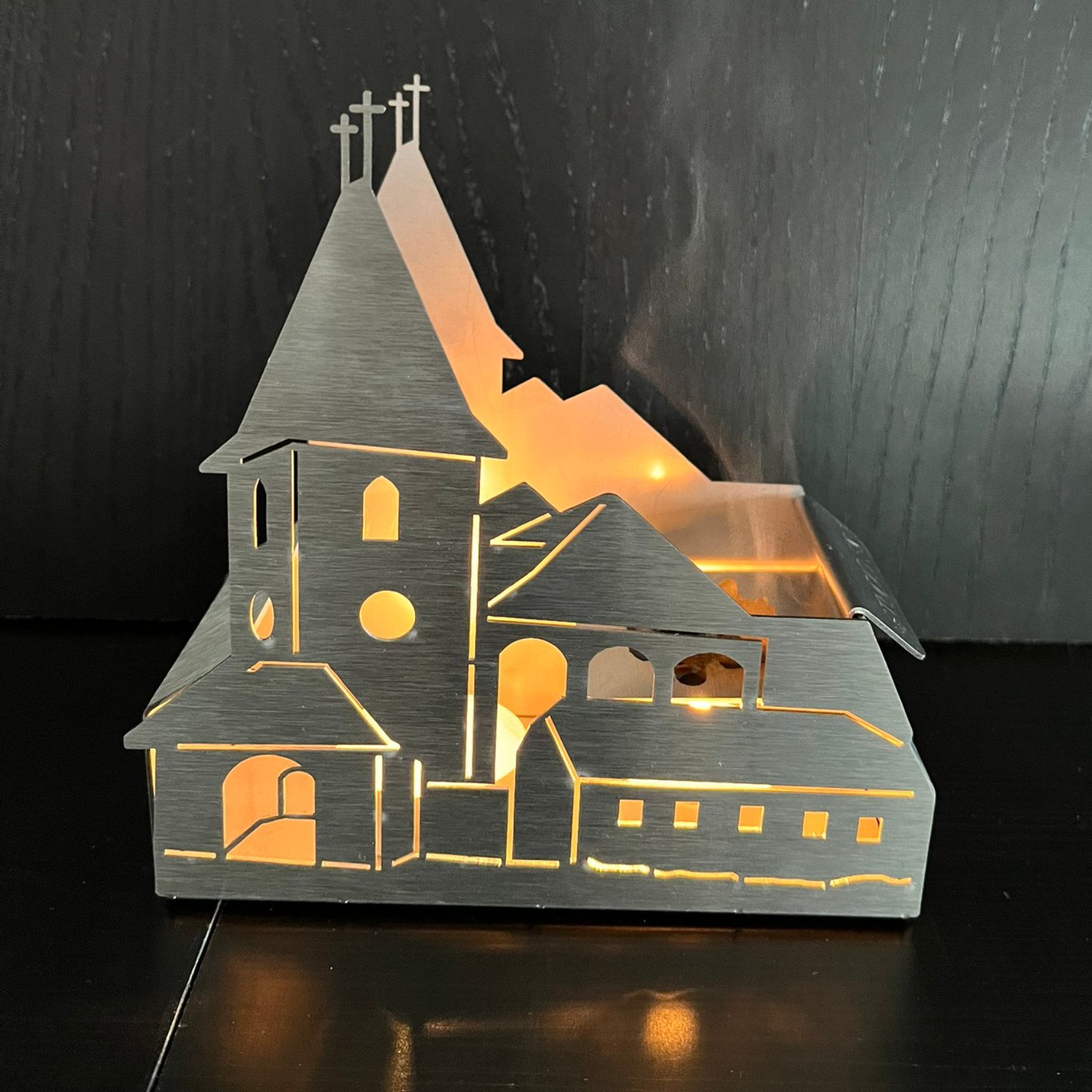 Die metallene Kirchensilhouette, von innen beleuchtet, wirft einen warmen Schein auf sich
