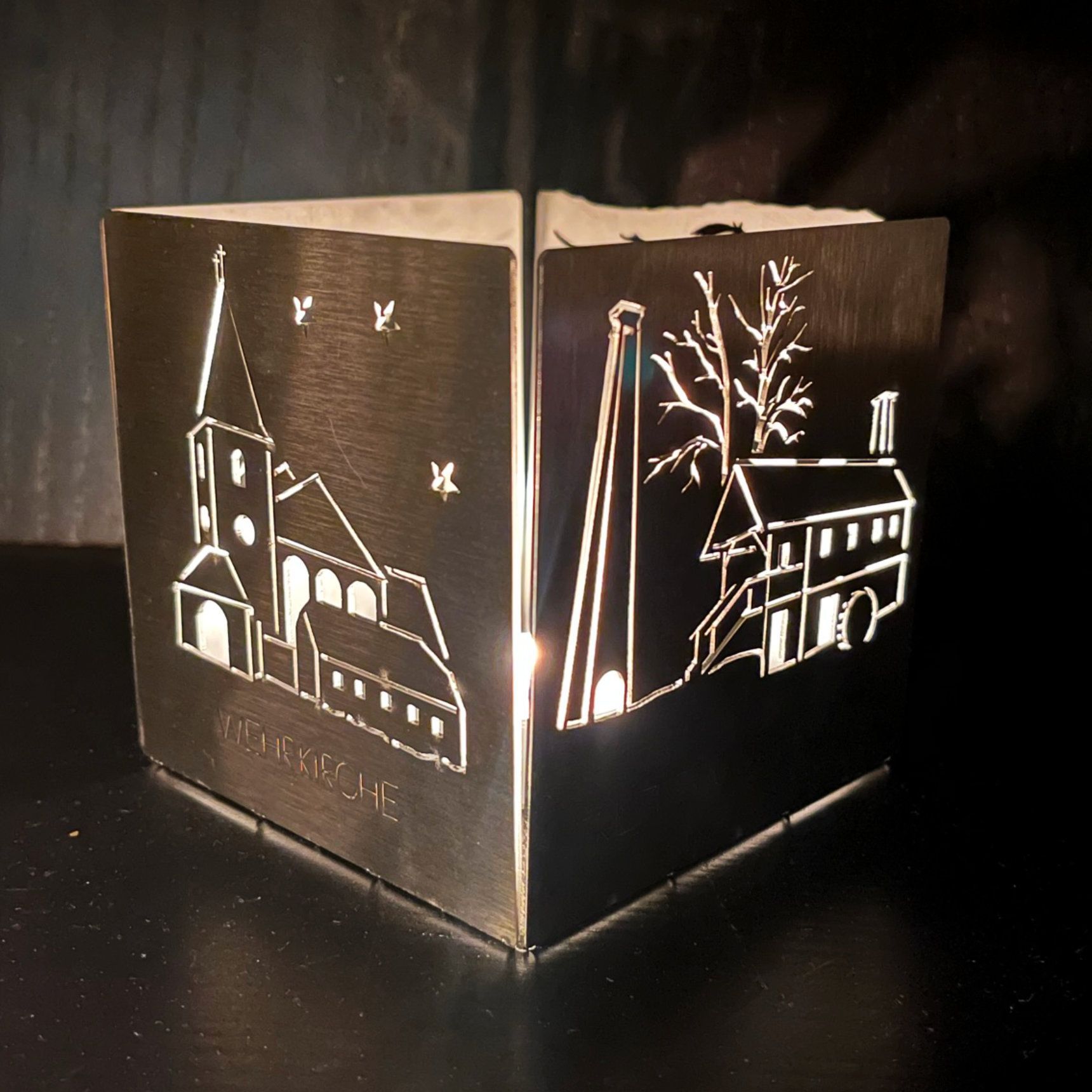 Metalllaterne mit ausgeschnittenen Szenen einer Kirche, eines Gebäudes und von Bäumen, die von innen beleuchtet sind.