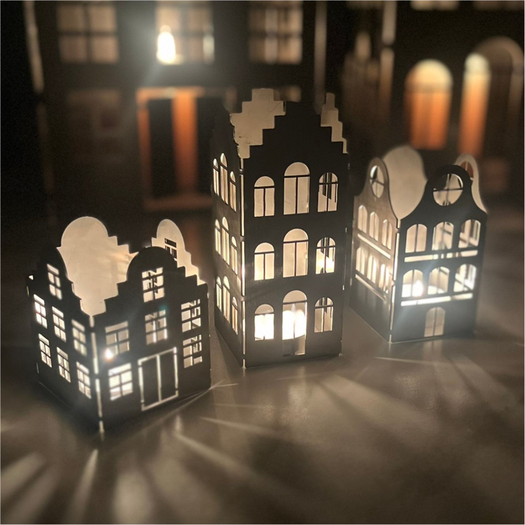 Drei beleuchtete, ausgeschnittene Papierhäuser werfen Licht auf einen Tisch. 