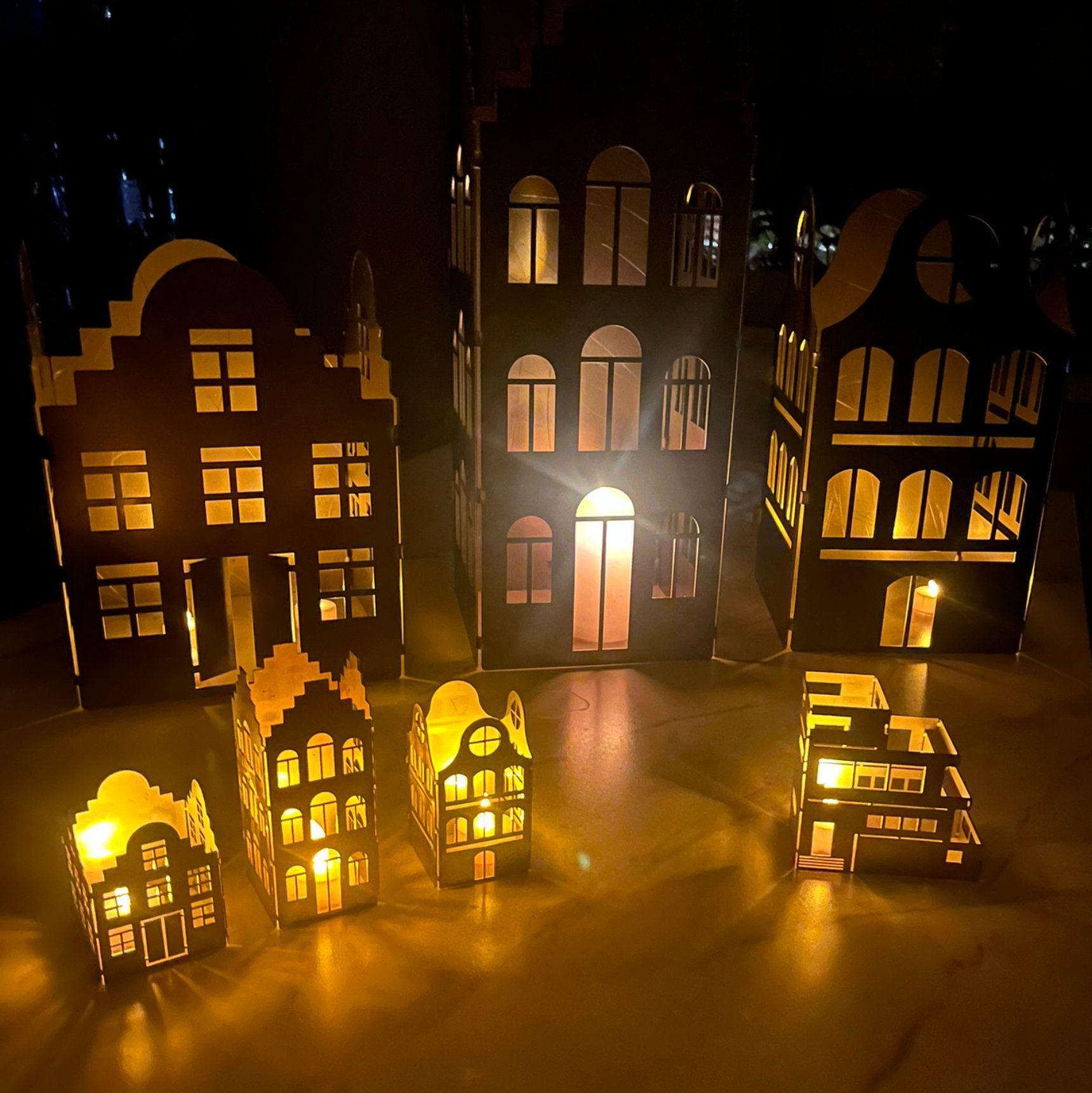 Beleuchtete Papplaternen in verschiedenen Größen und Ausführungen werfen ein warmes Licht vor einem dunklen Hintergrund.