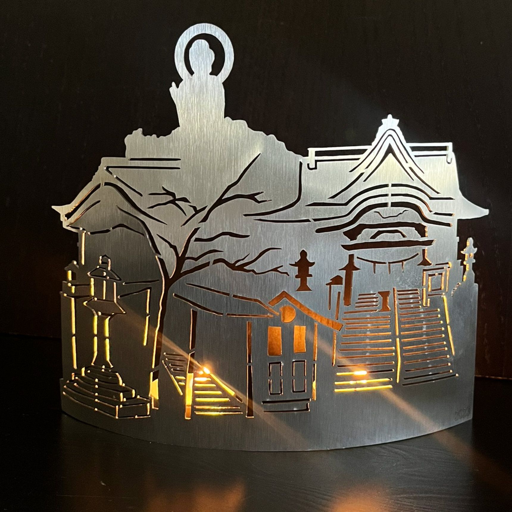 Metallausschnitt, der einen japanischen Tempel mit einer Buddha-Figur darstellt, der von hinten beleuchtet wird