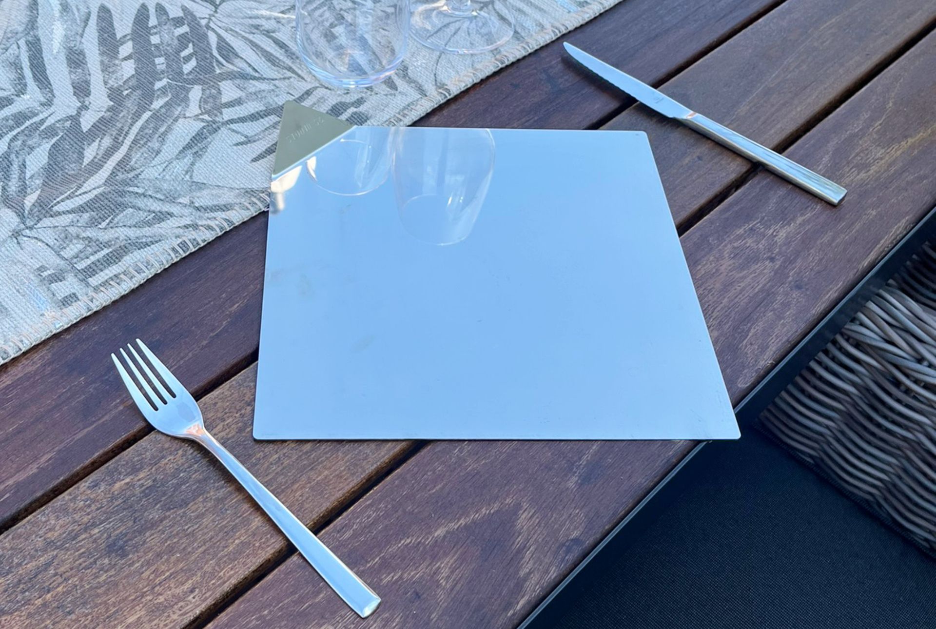 Silberbesteck (Gabel und Messer) neben einem weißen Quadrat auf einem Holztisch. Im Hintergrund ist ein Tuch zu sehen.