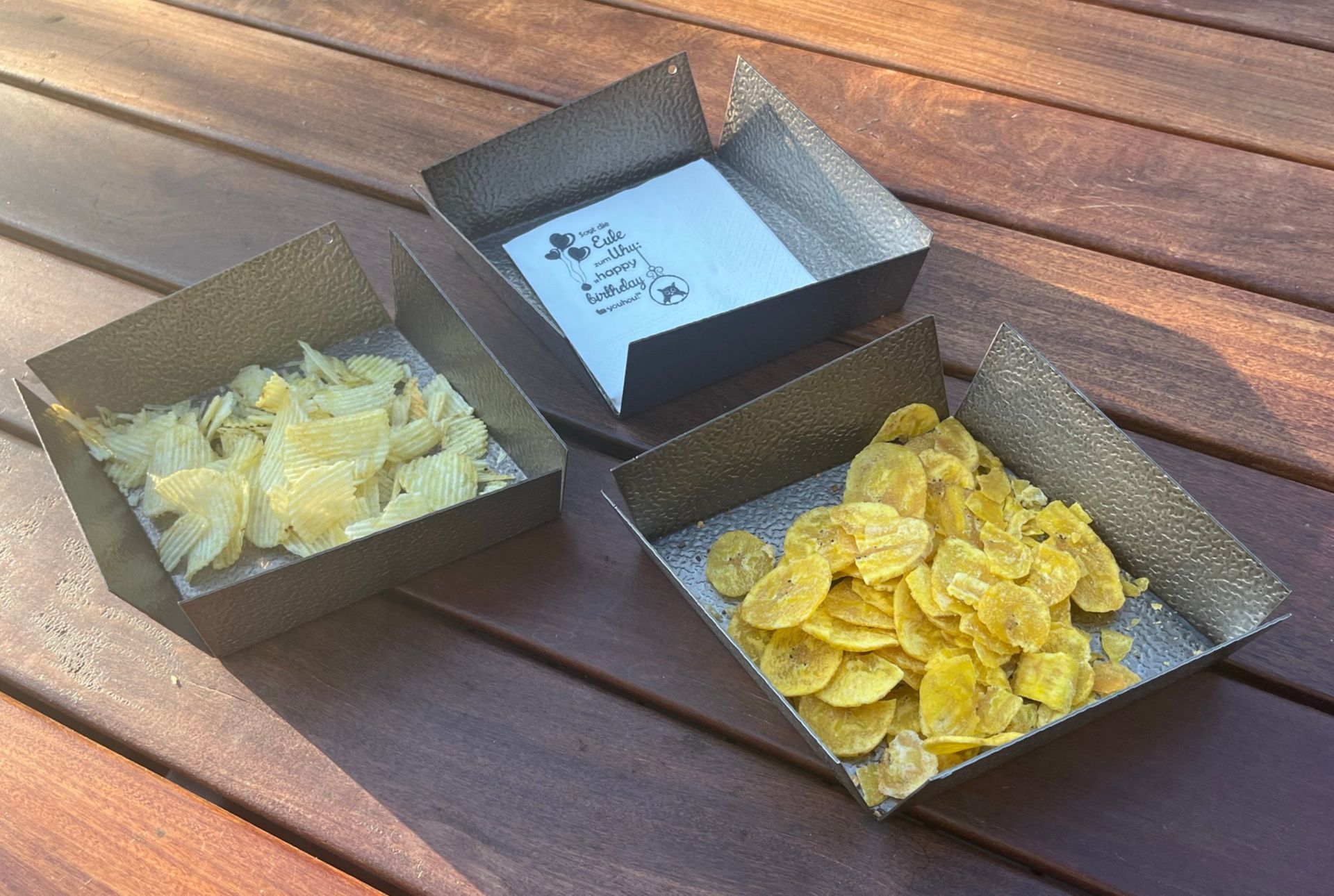 Drei quadratische Metallbehälter auf einer Holzoberfläche mit Chips
