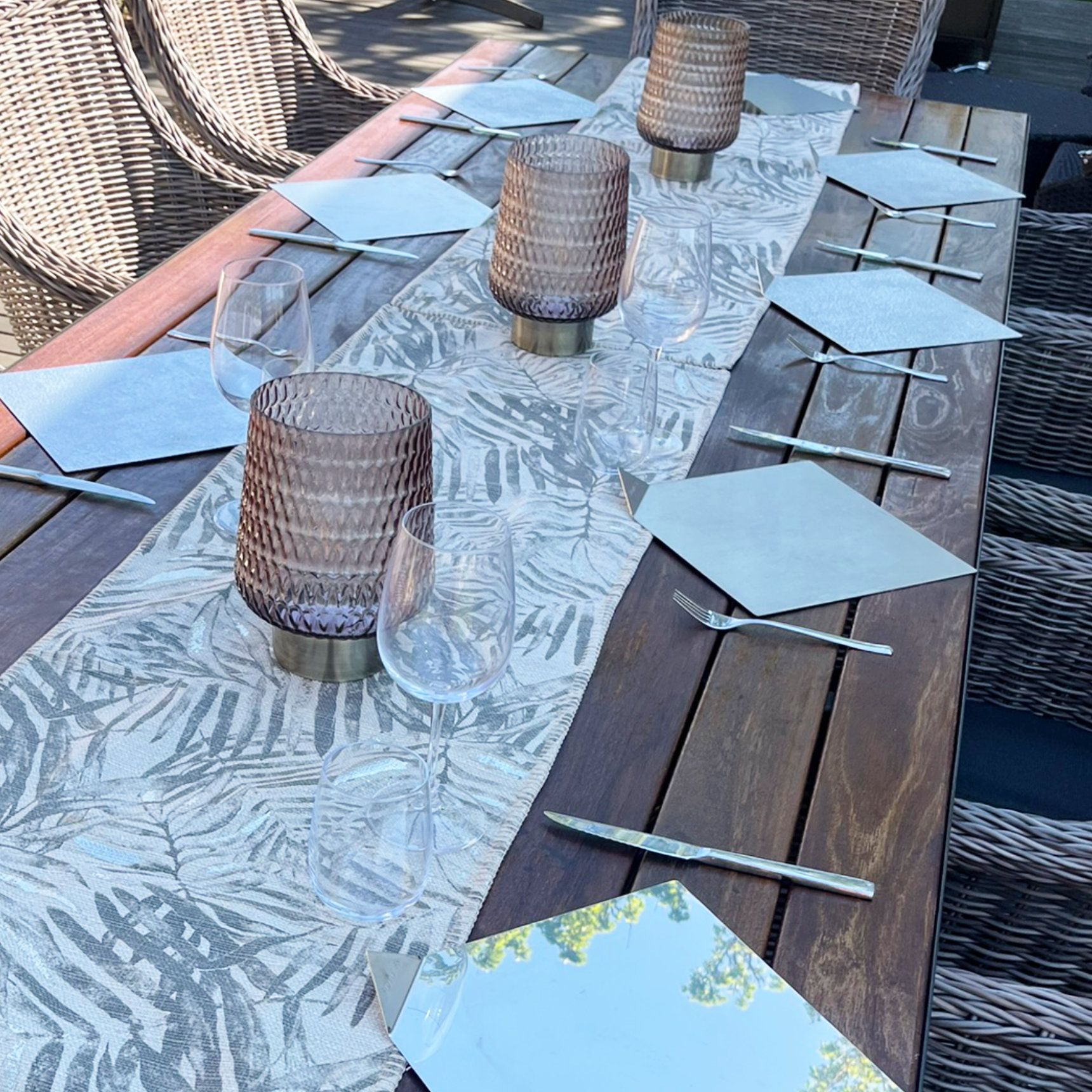 Gartentischgarnitur mit Gedecken, Blumenläufer und Laternen.