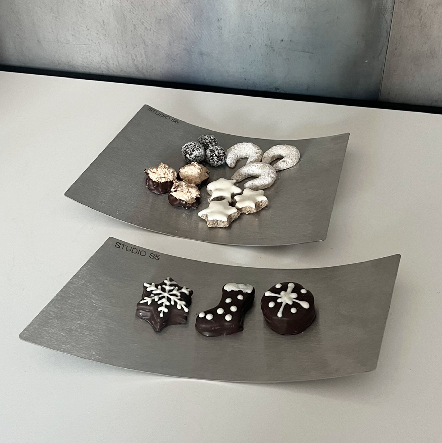 Zwei silberne, quadratische Schalen mit Weihnachtsplätzchen auf weißem Grund.