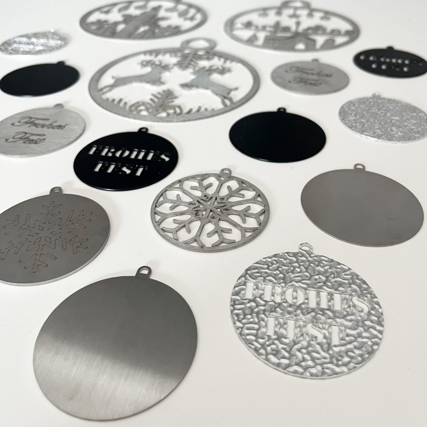 Verschiedene Metallornamente, darunter Schneeflocken und Schriftzüge, liegen auf einer weißen Fläche.