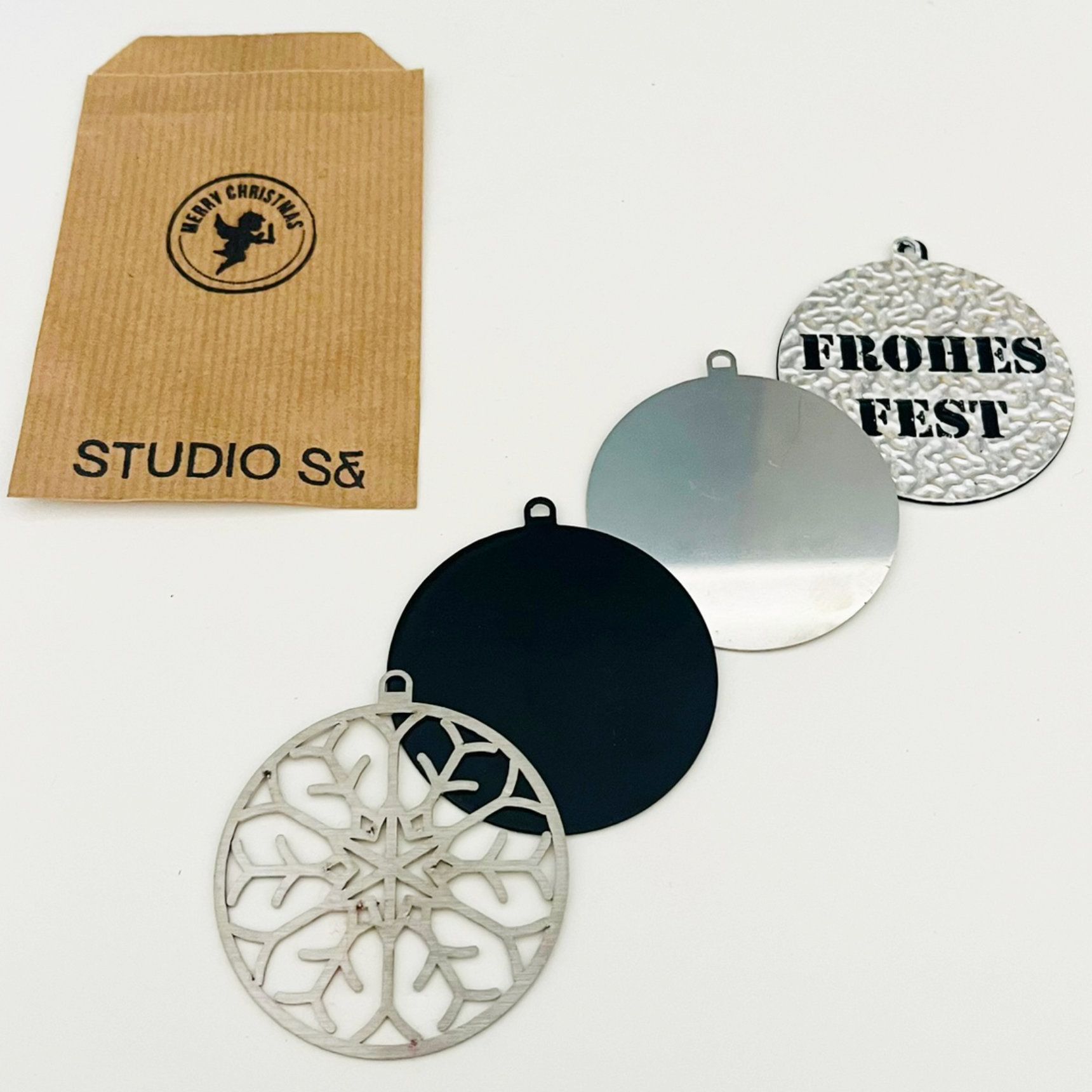 Weihnachtsschmuck in einem Bastelumschlag: Schneeflocke, schwarz, silber, „Frohes Fest“.