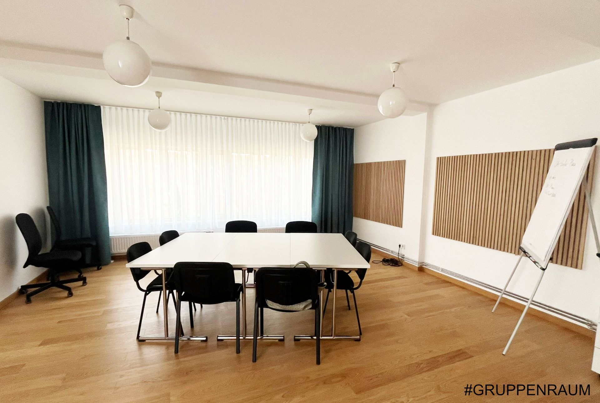 Besprechungsraum mit Tisch, Stühlen, Whiteboard, Holzvertäfelung, Vorhängen und Deckenbeleuchtung.