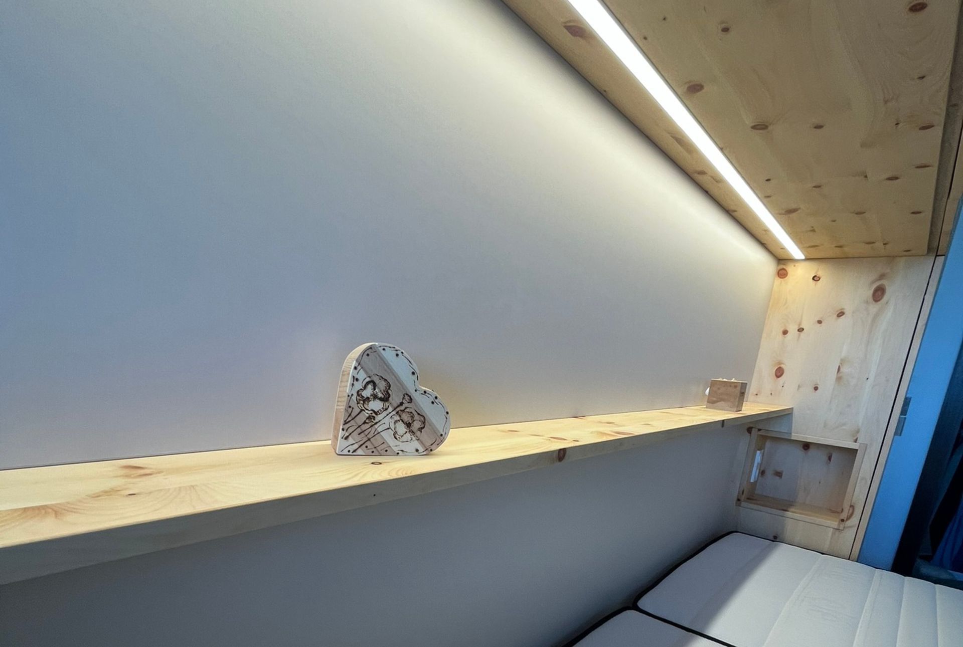 Holzregal mit einem herzförmigen Objekt darauf, unter einem LED-Lichtstreifen. Innenansicht.