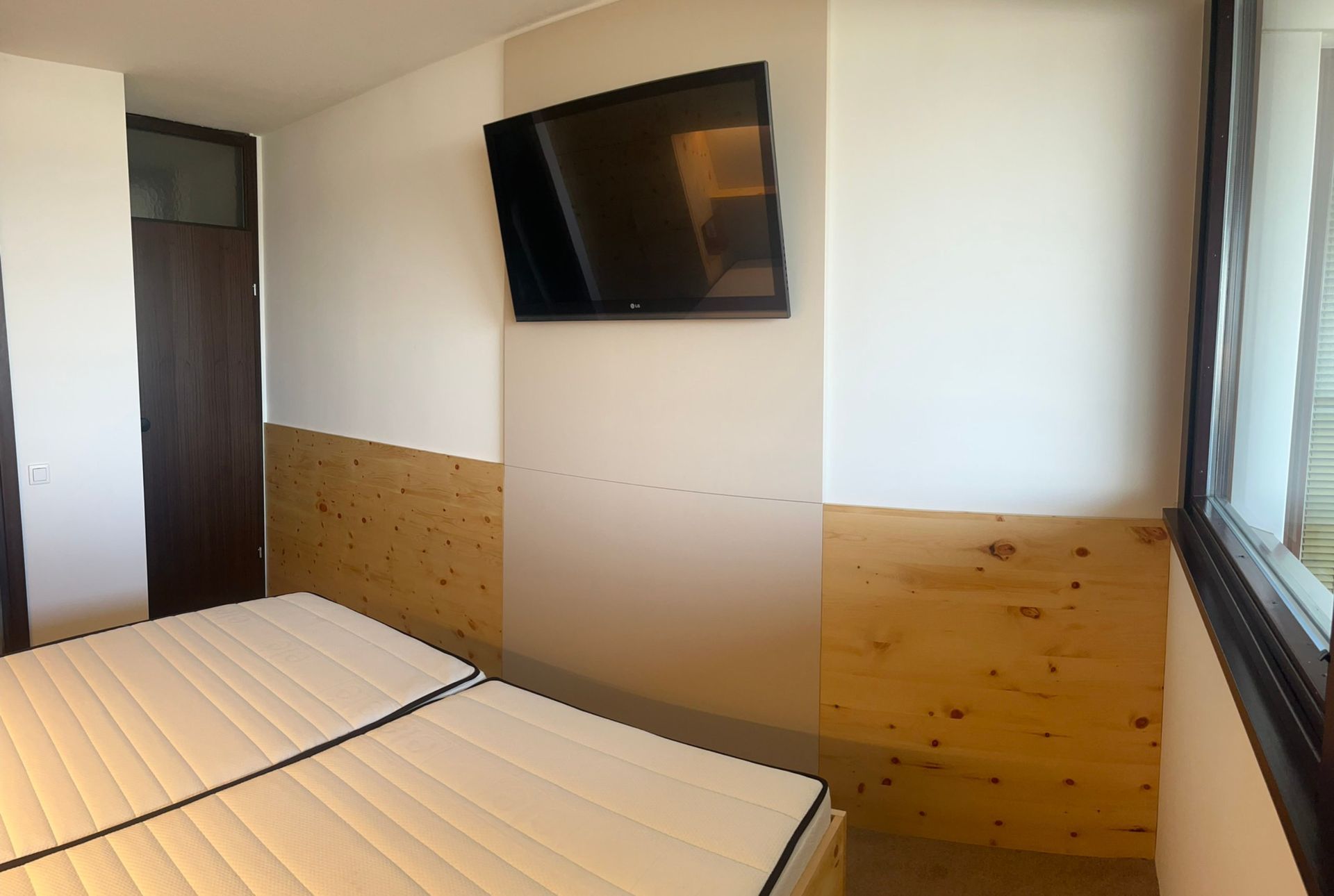 Schlafzimmer mit Bett, Wandfernseher, Holzvertäfelung und Tür.
