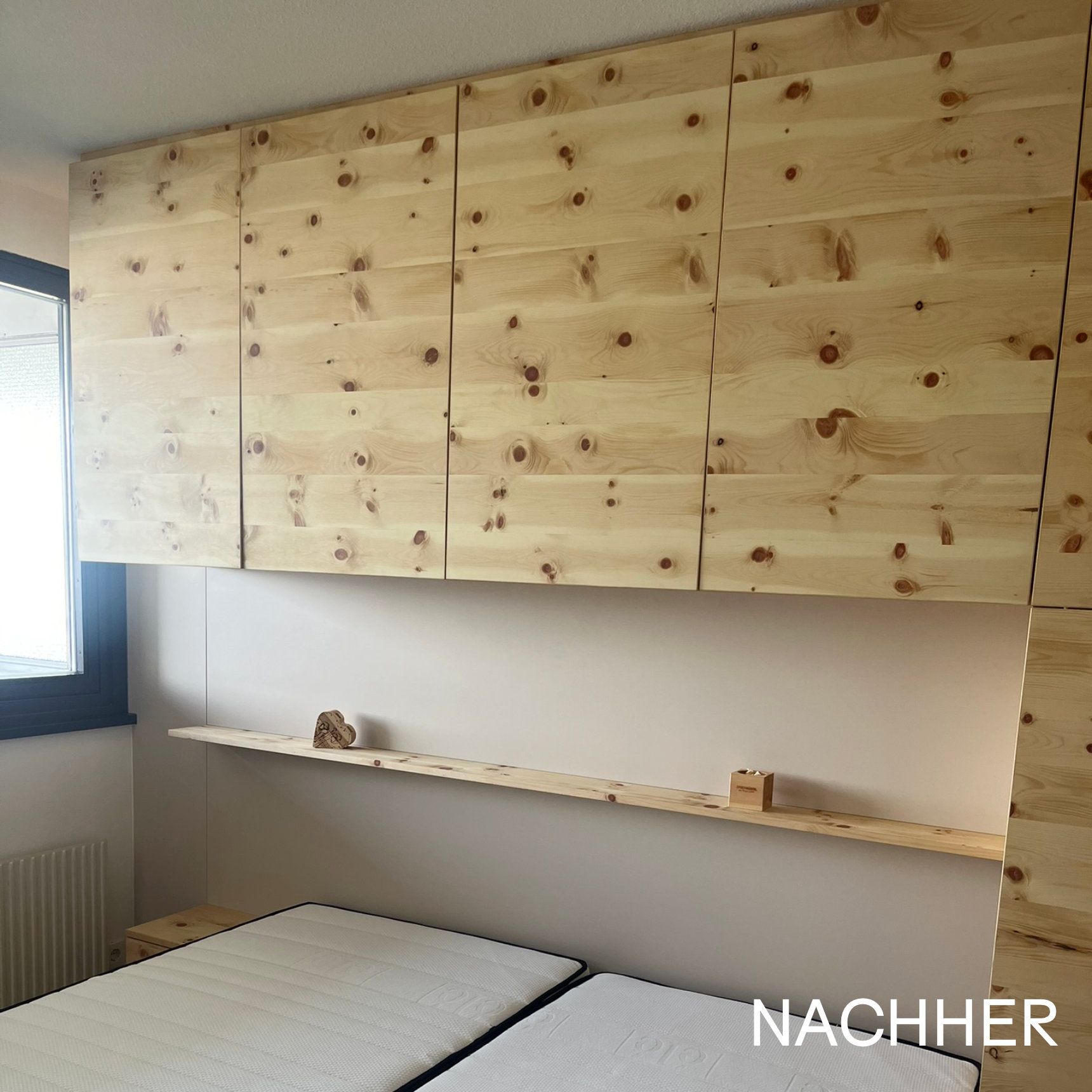 Hölzerne Aufbewahrungsschränke über einem Bett, mit einem Regal. Helle Holzfarbe. Schriftzug „NACHHER“.