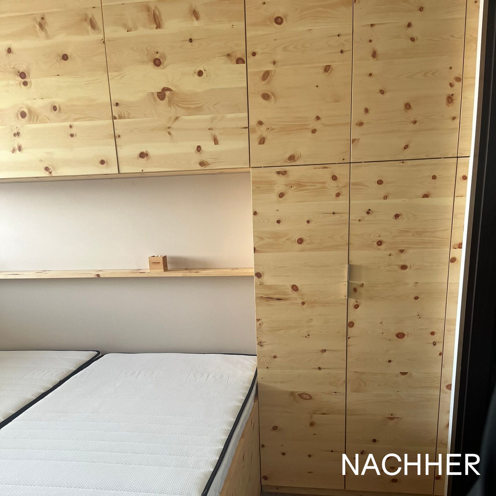 Einbauschränke aus Holz im Schlafzimmer mit Hängeschränken und seitlichem Kleiderschrank. Helles Holz und neutral getönte Wand im Bereich des Bettes.