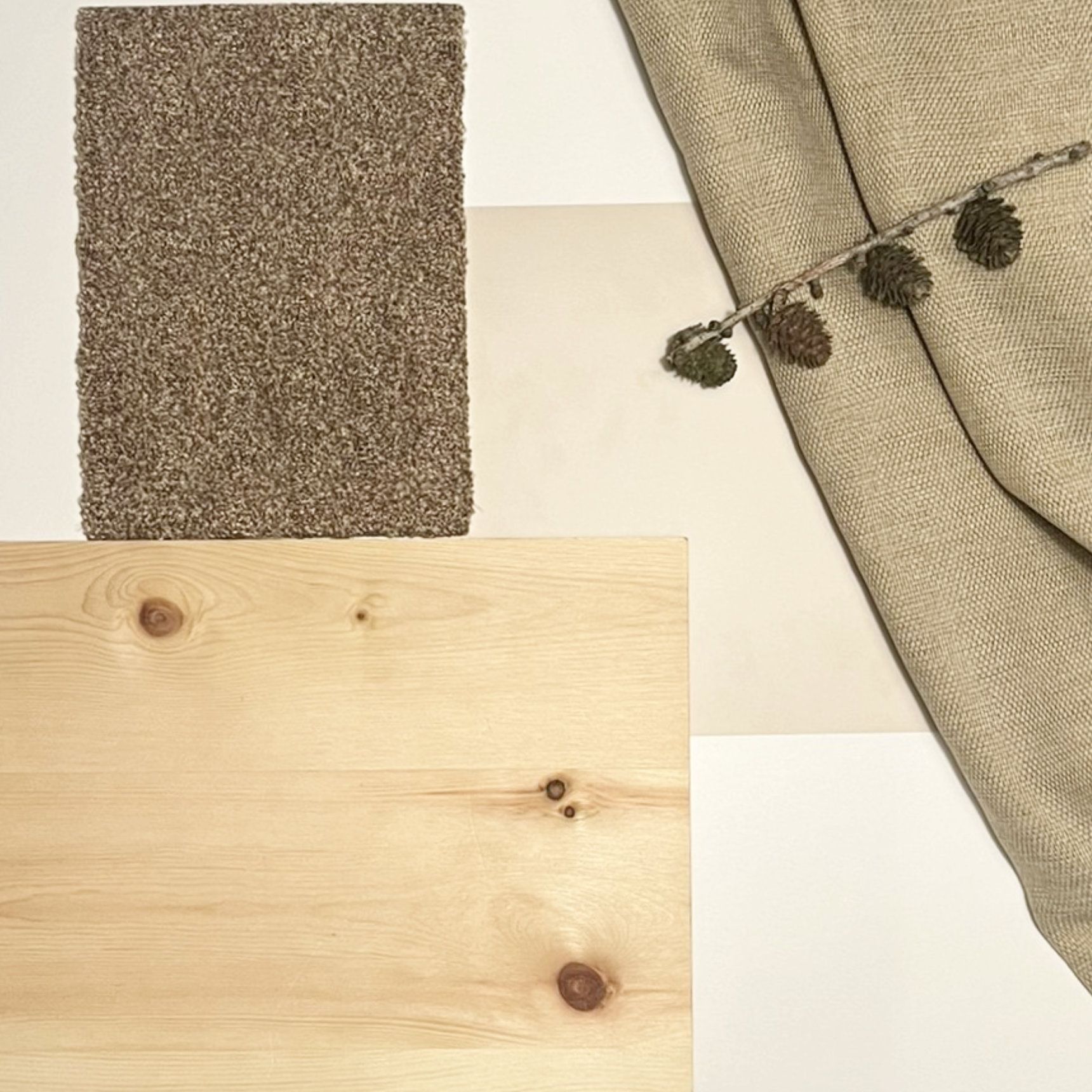Holzoberfläche mit neutralen Textilien, ein kleiner Ast mit Tannenzapfen und ein strukturiertes braunes Quadrat.