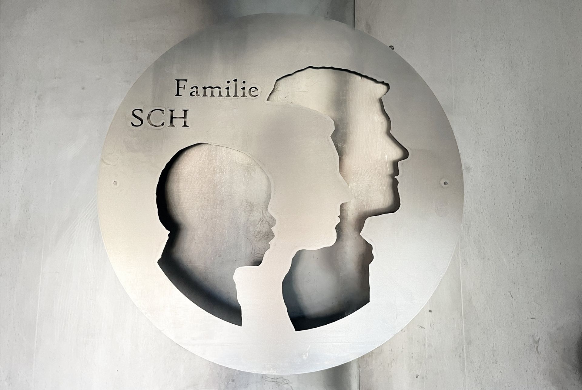 Ein kreisrunder Metallausschnitt mit den Silhouetten von Menschen, mit der Aufschrift „Familie SCH“.