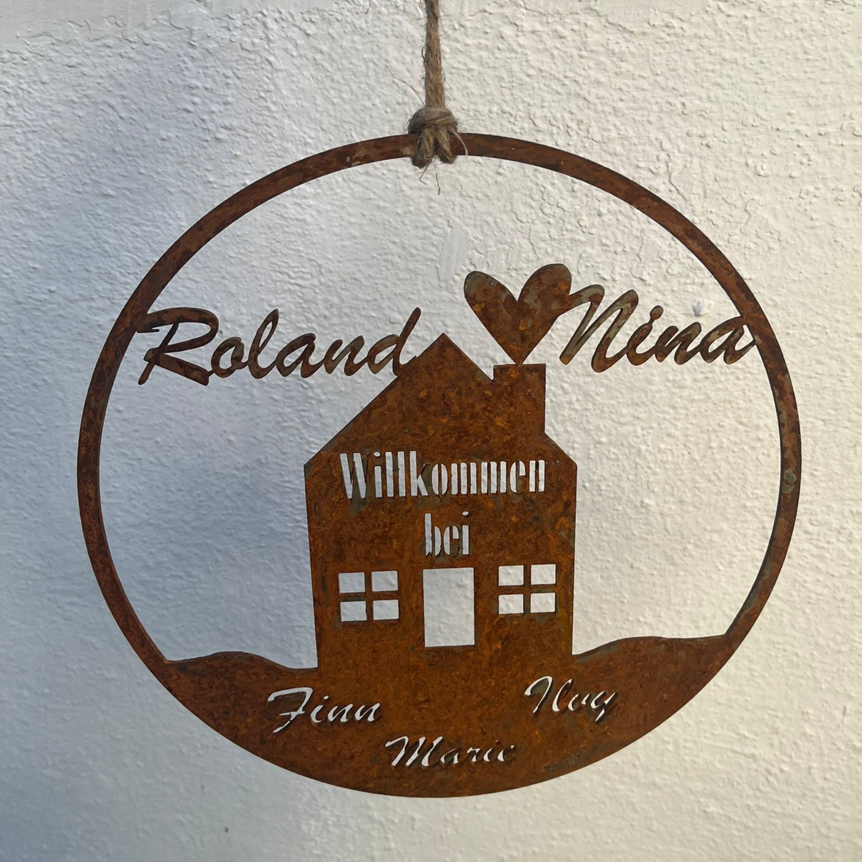 Rostiges Willkommensschild aus Metall mit den Namen „Roland“ und „Nina“, einem Haus und dem Schriftzug „Willkommen bei…“