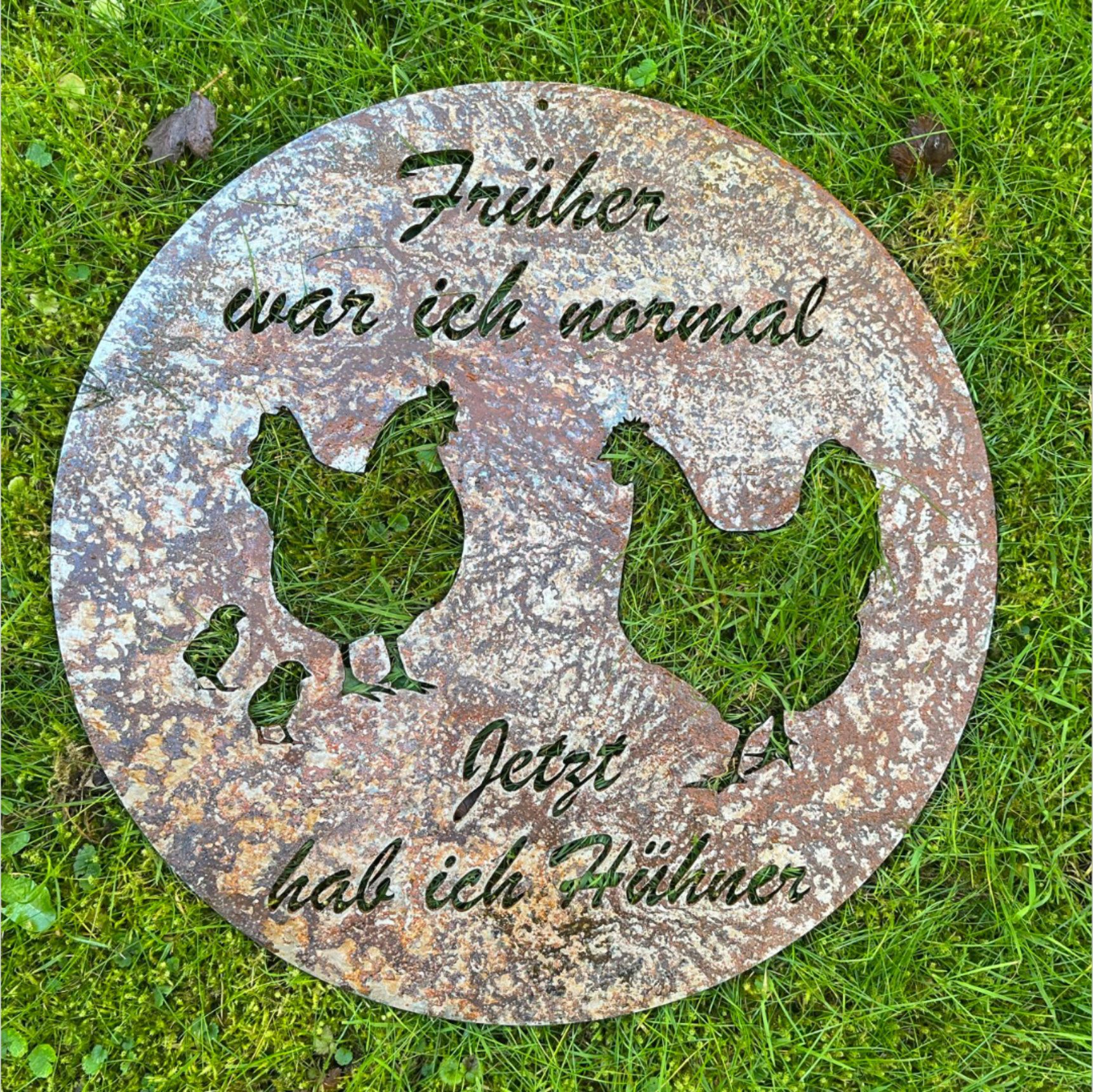 Runder Gartenstein aus Metall mit Hühner-Ausschnitten und deutschem Text: „Früher war ich normal, jetzt habe ich Hühner.“