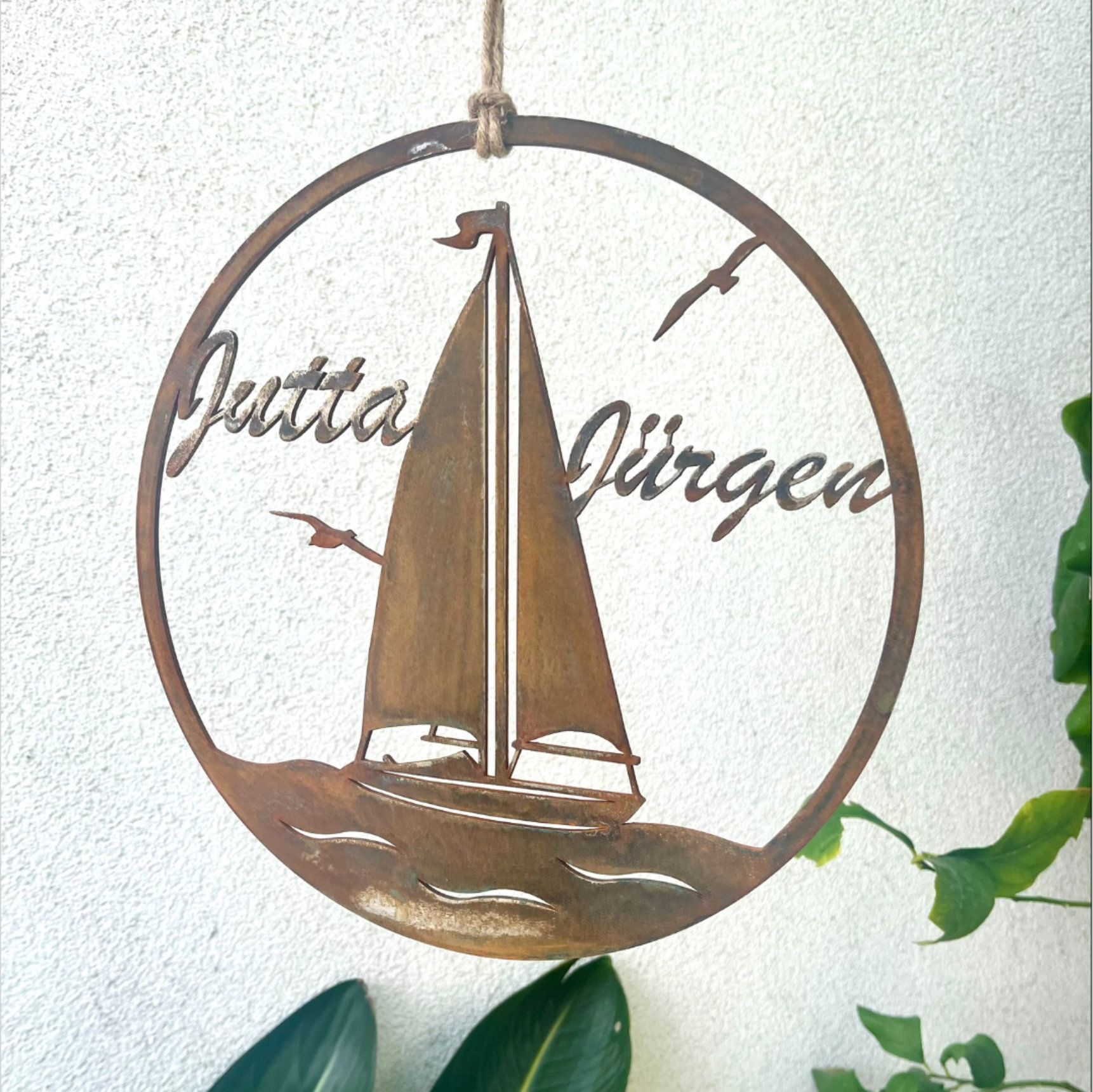 Metallenes Segelbootschild mit der Aufschrift „Jutta Jürgen“ und Möwen, das an einem Seil hängt.